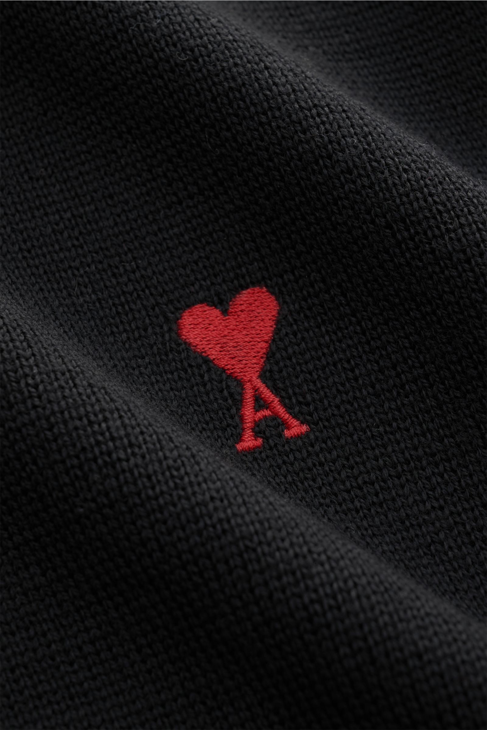 Nahaufnahme des Ami Paris Merino Rundhalspullover schwarz mit feinem Strickbild und rotem Logo-Stitching auf der Brust, reine Merinowolle.