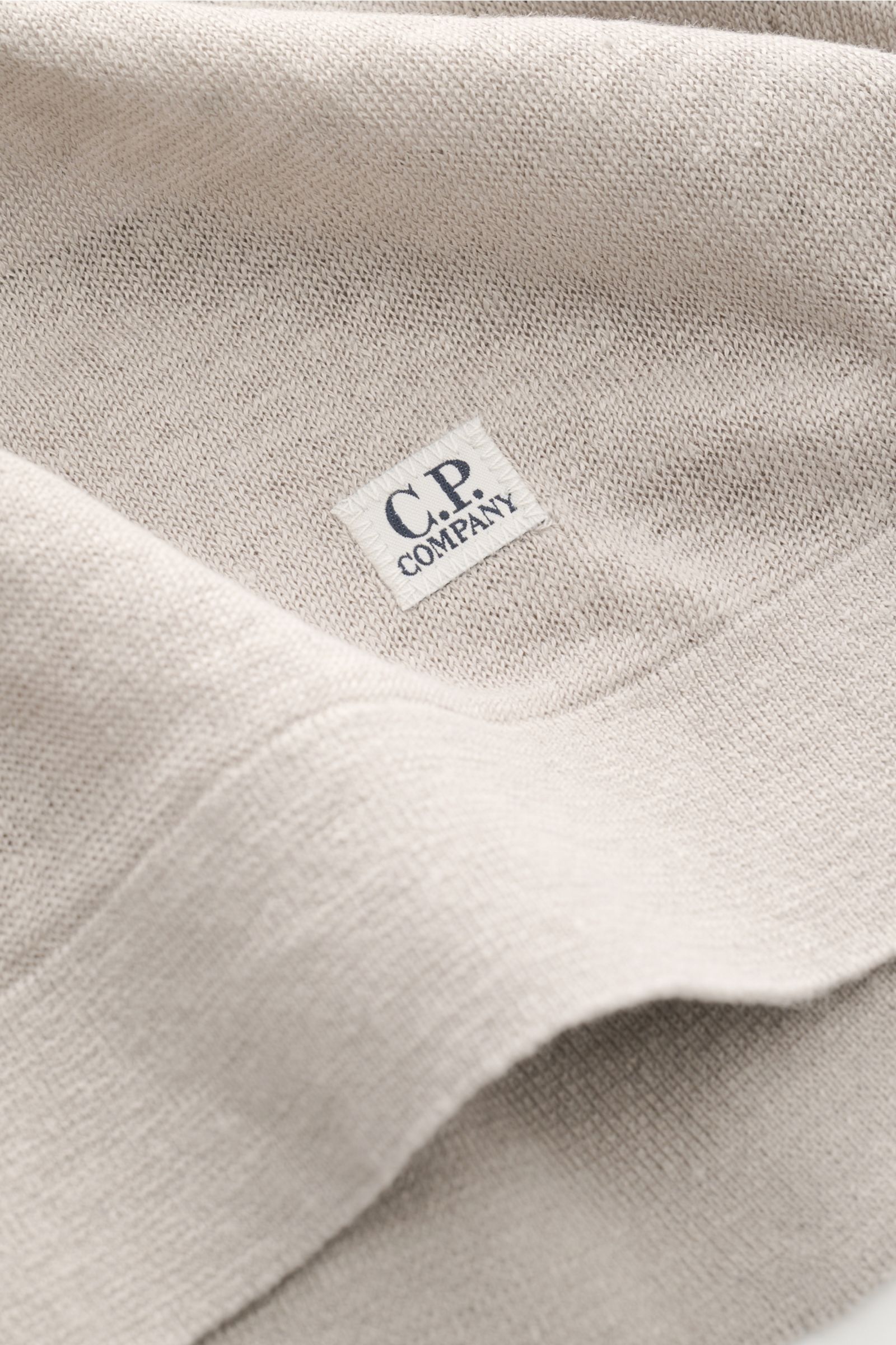 Nahaufnahme des C.P. Company Kurzarmpullovers grau aus feinstem Leinenstrick, weicher Griff, feines Strickbild, mit kleinem Weblabel am Saum.