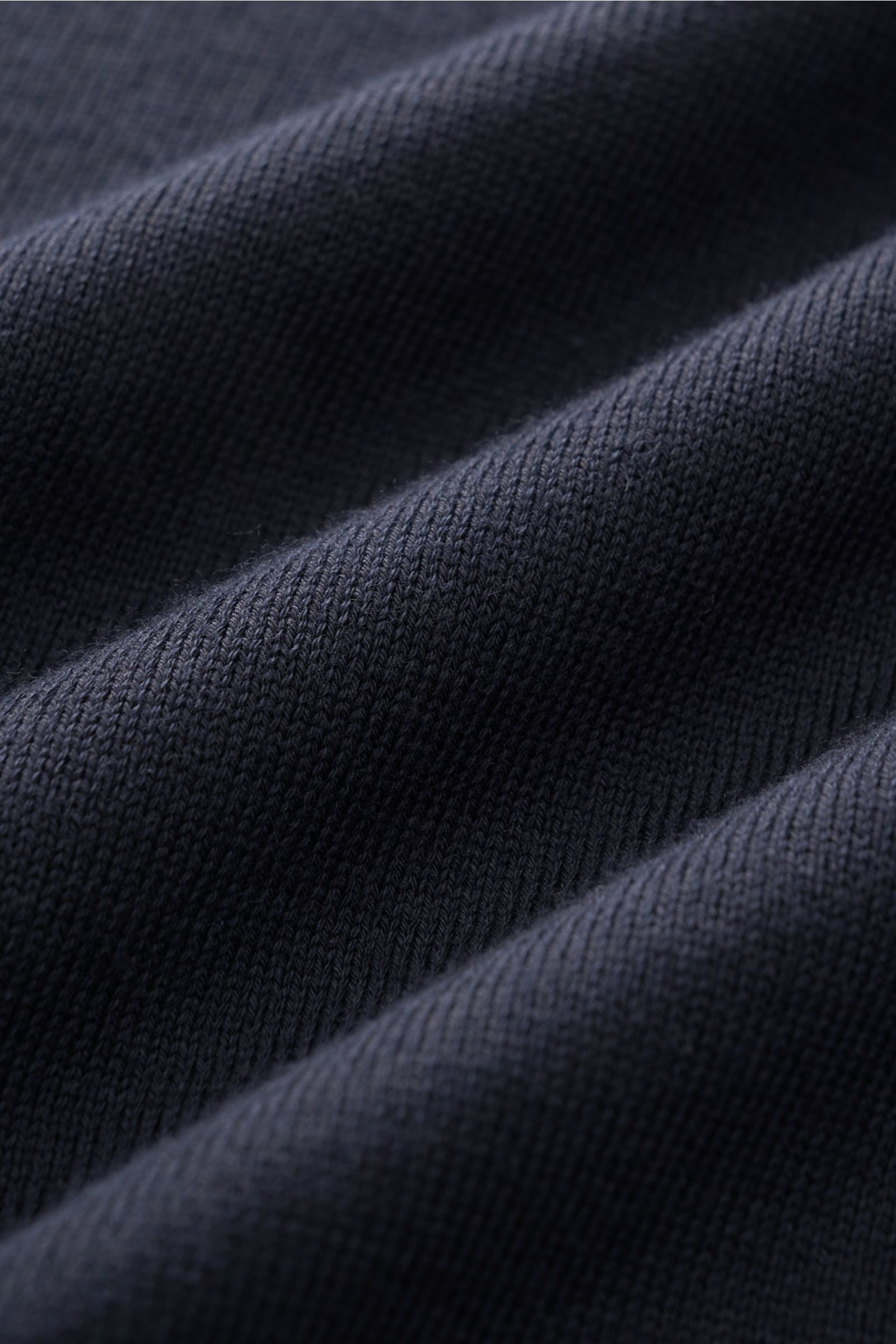 Nahaufnahme des fein gestrickten Stoffes des C.P. Company Rundhalspullover navy, fotografiert aus schräger Perspektive mit Fokus auf die weiche Baumwollstruktur. 