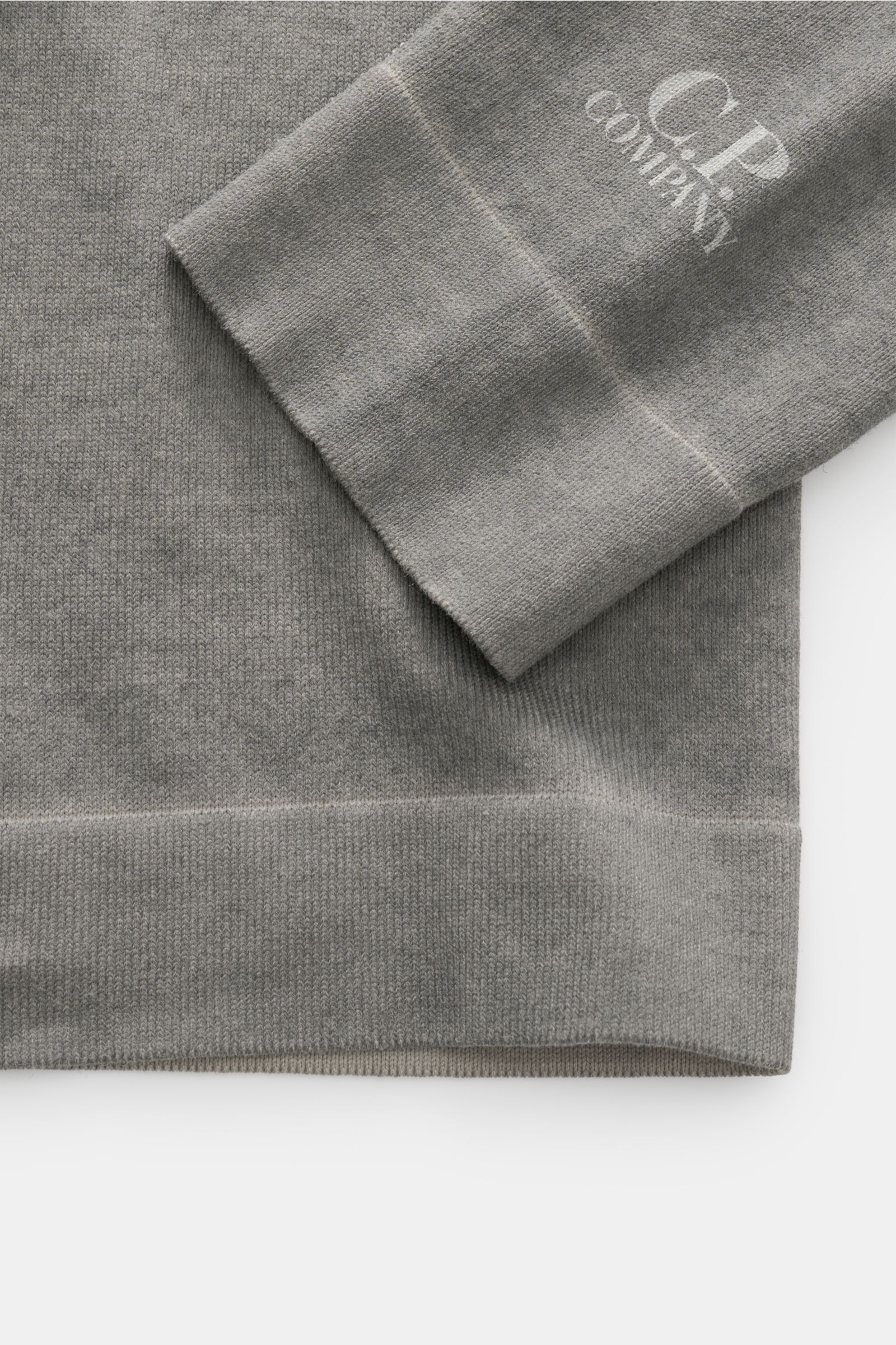 C.P. Company Rundhalspullover grau aus reiner Baumwolle mit weichem Griff, Garment-Dyed-Design, feinem Strickbild, Regular Fit, Rundhalsausschnitt, Logo-Print am Ärmelsaum und Rippbündchen, Detailfoto von Ärmel und Saum.