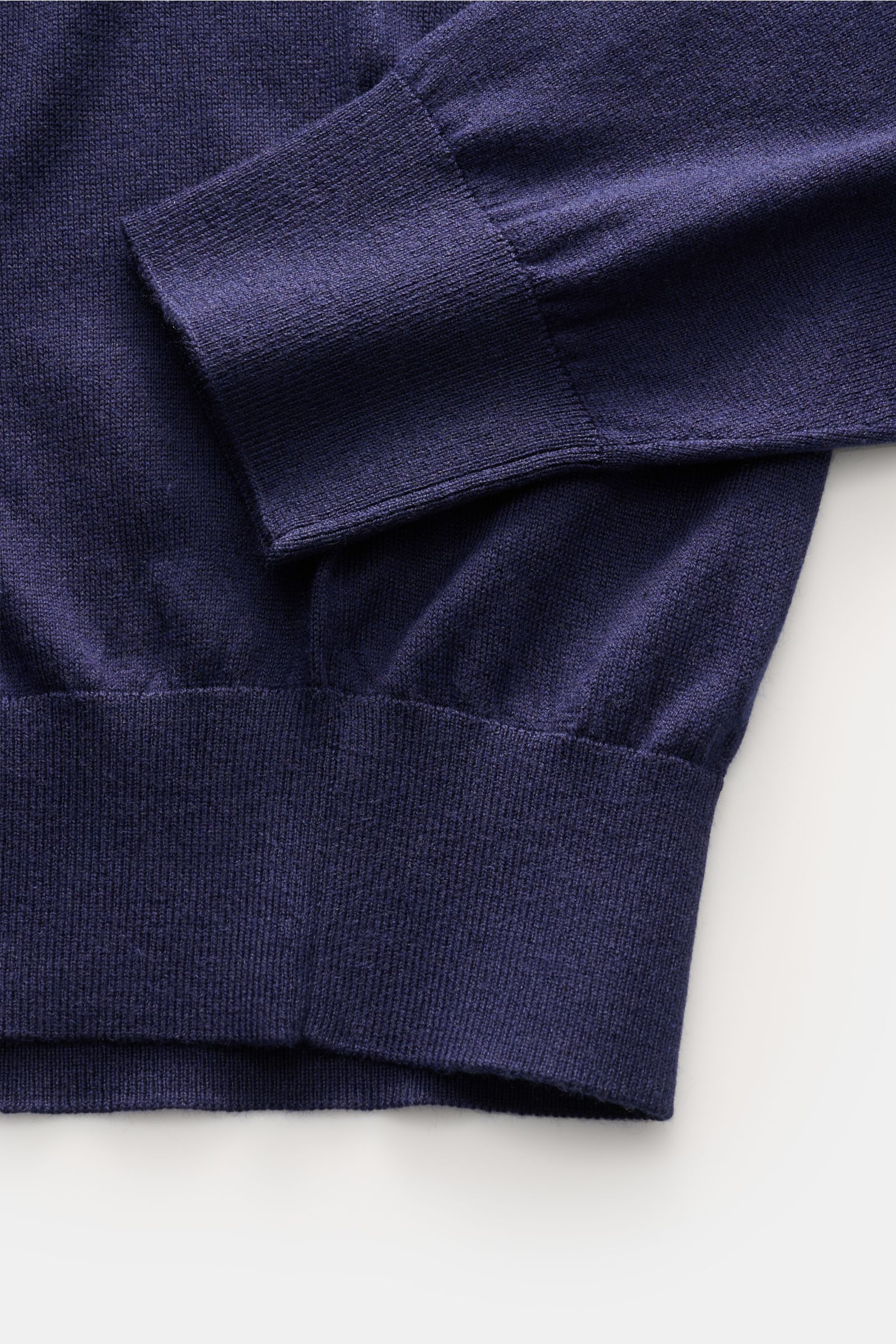Close-up image from above of the cuff and hem details of the Della Ciana Feinstrick-Rundhalspullover 'Girocollo' navy, showcasing its slim fit, soft mix of silk and cashmere, fine knit texture, round neckline, and comfortable ribbed cuffs and waistband. 