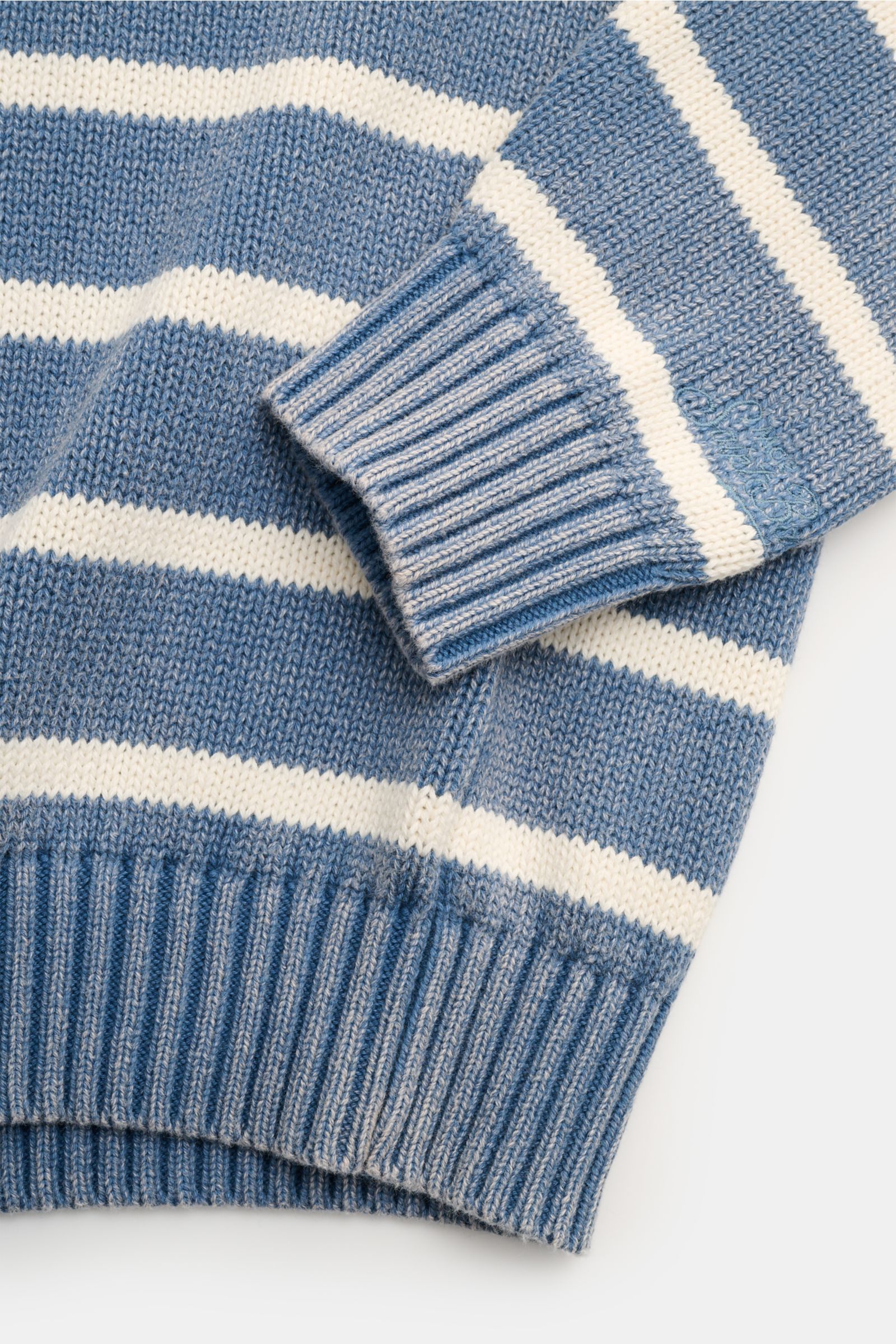 Close-up view of the MC2 Saint Barth Crew neck jumper 'Sydney Cotton' smoky blue/cream striped, showing the ribbed cuff with tonal logo stitching and classic striped pattern. Dancing barefoot on a table: The 'Sydney Cotton' crew neck jumper from MC2 Saint