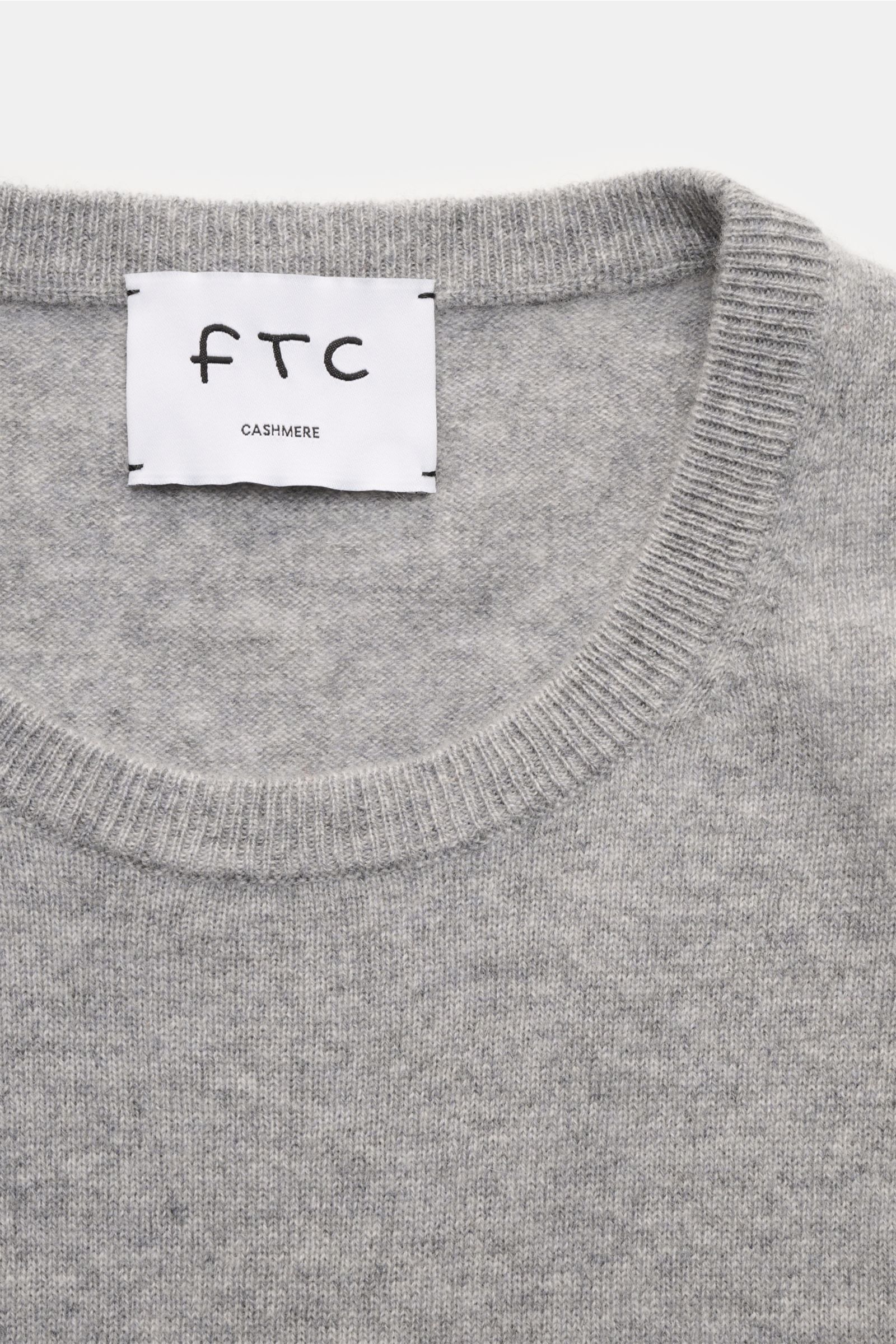 Close-up top view of FTC Cashmere Rundhalspullover grau meliert, showing the round neckline and label on soft, fine-knit grey melange cashmere fabric.

Das Tragegefühl ultraweicher Cashmere-Qualität lässt diesen zeitlosen Rundhalspullover vom nachhalti