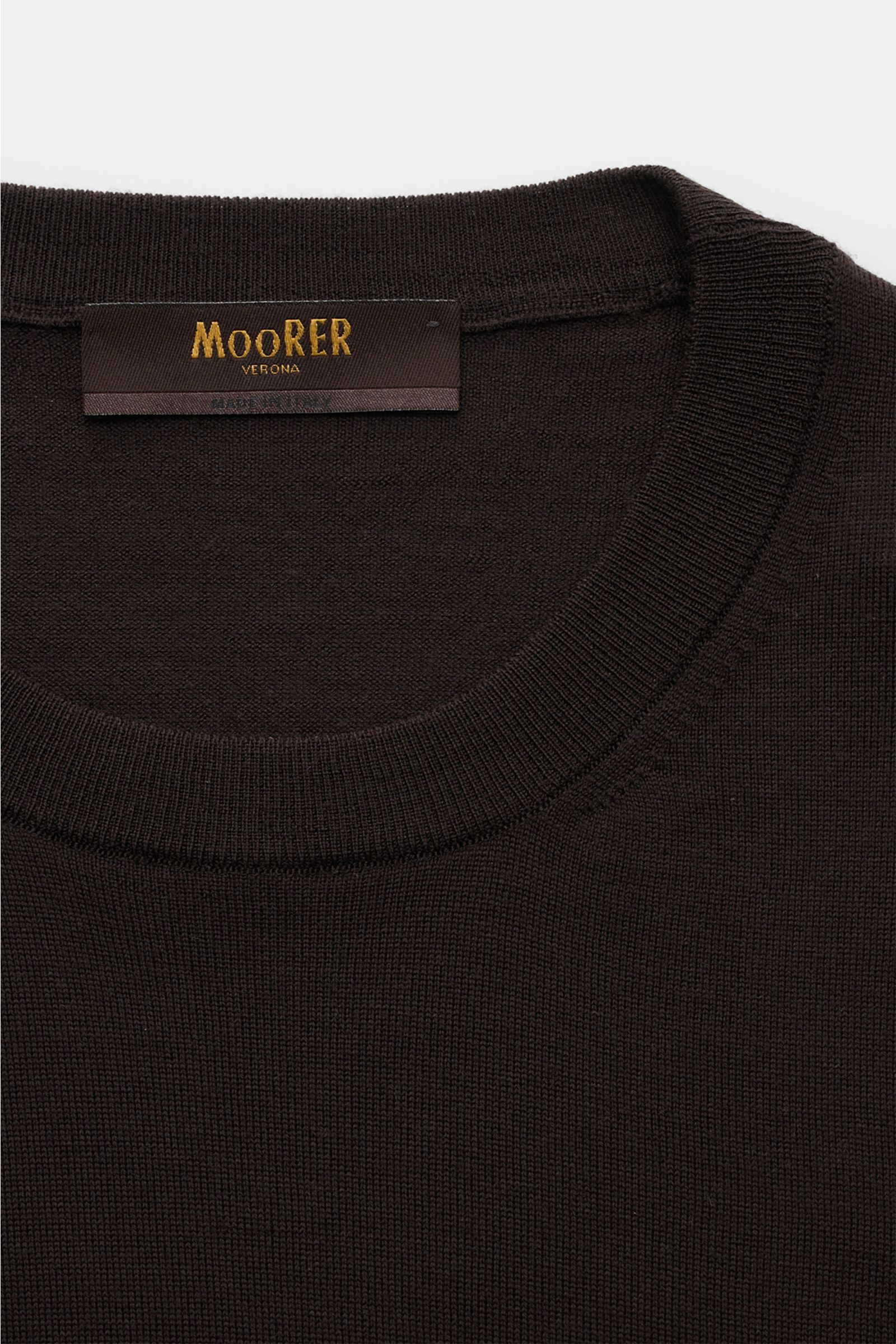 Close-up, top-down view of the Moorer Rundhalspullover 'Orvieto' dunkelbraun, showcasing pure new wool, soft feel, very fine knit, slim fit, round neckline, and comfortable ribbed cuffs.  
Puristische Raffinesse: In feinem Schurwollstrick gefertigt, verbi