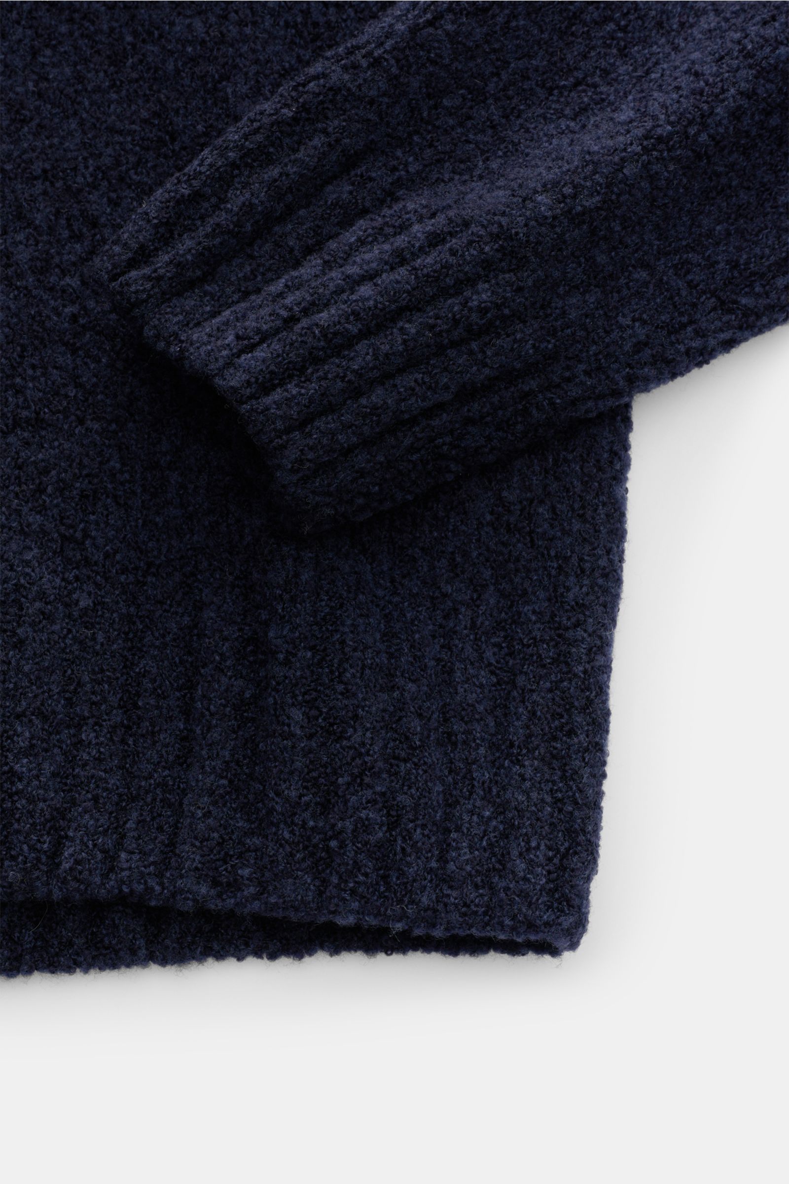 Close-up front view of the sleeve and hem of the 04651/ A trip in a bag Mock neck jumper 'Grainy' navy melange showing textured, warm wool blend bouclé knit with ribbed collar and wide ribbed bands. For modern looks: The jumper 'Grainy' by 04651/ A TRIP I