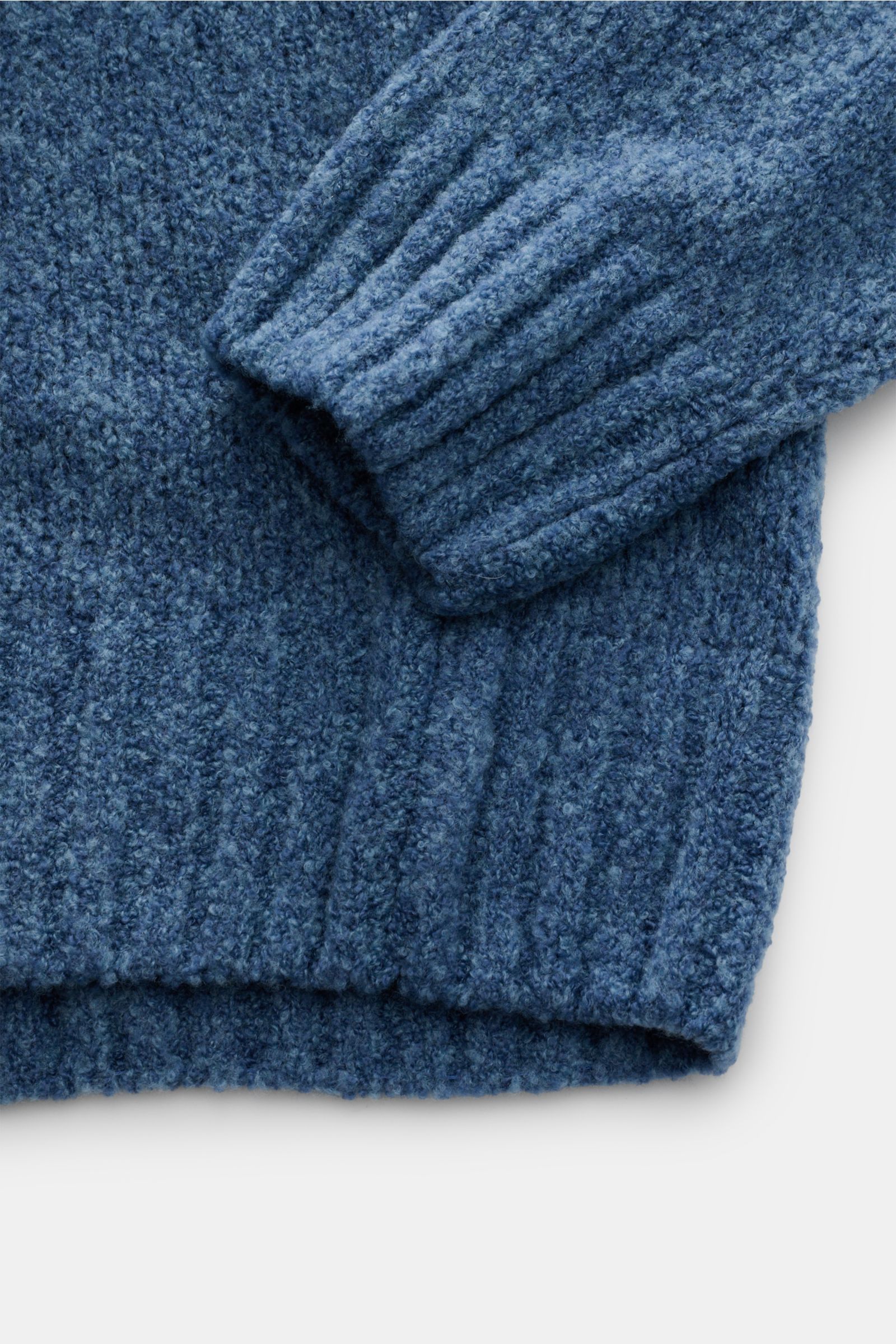 Close-up image of the sleeve and hem of the 04651/ A trip in a bag Mock Neck Pullover 'Grainy' rauchblau, showing its textured bouclé knit fabric and ribbed cuffs, photographed from above. Für moderne Looks: Der Pullover 'Grainy' von 04651/ A TRIP IN A BA