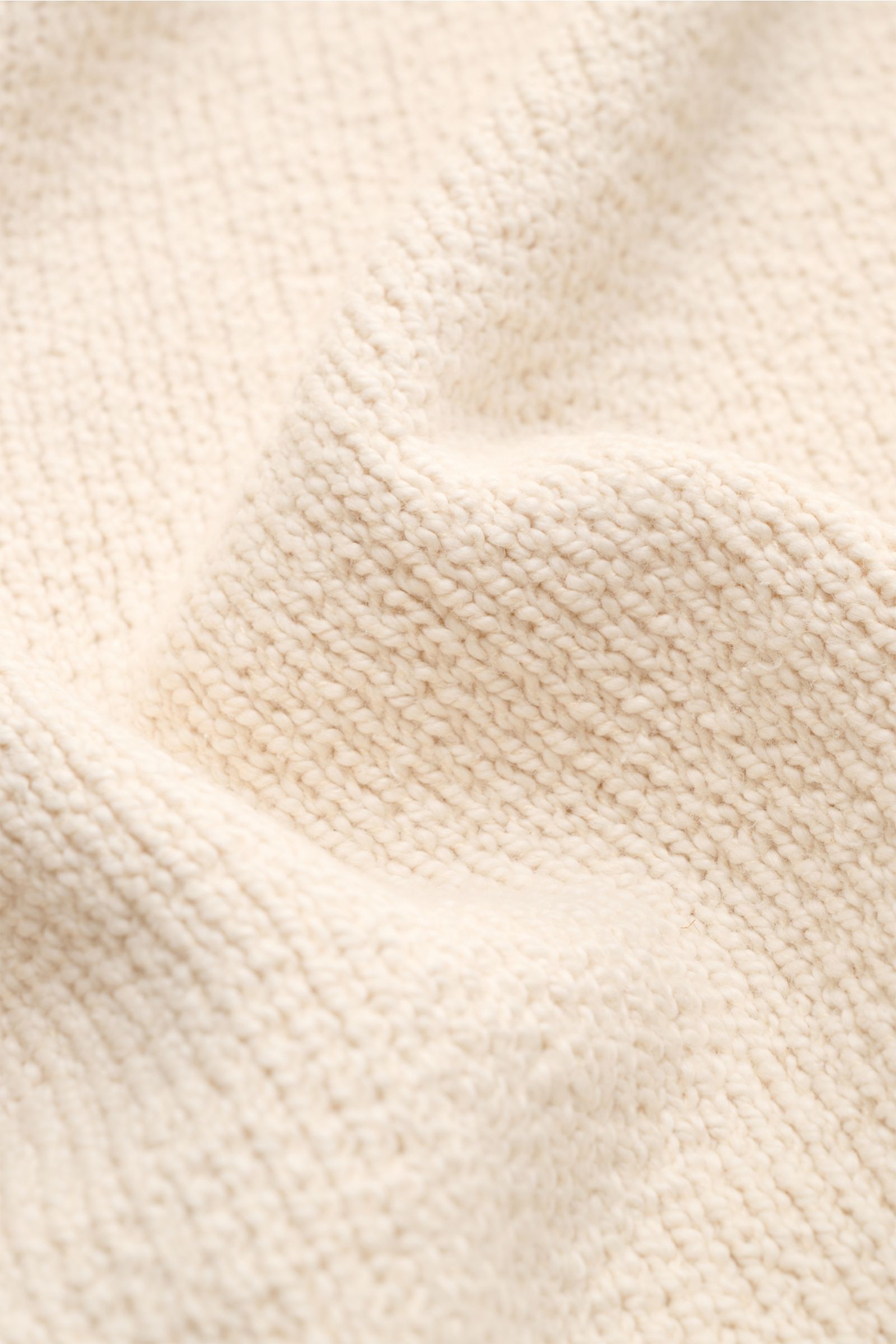 Nahaufnahme der weichen Bouclé-Struktur des 04651/ A trip in a bag Rundhalspullover 'Boucle Crew' beige, Detailfoto aus schräger Perspektive.