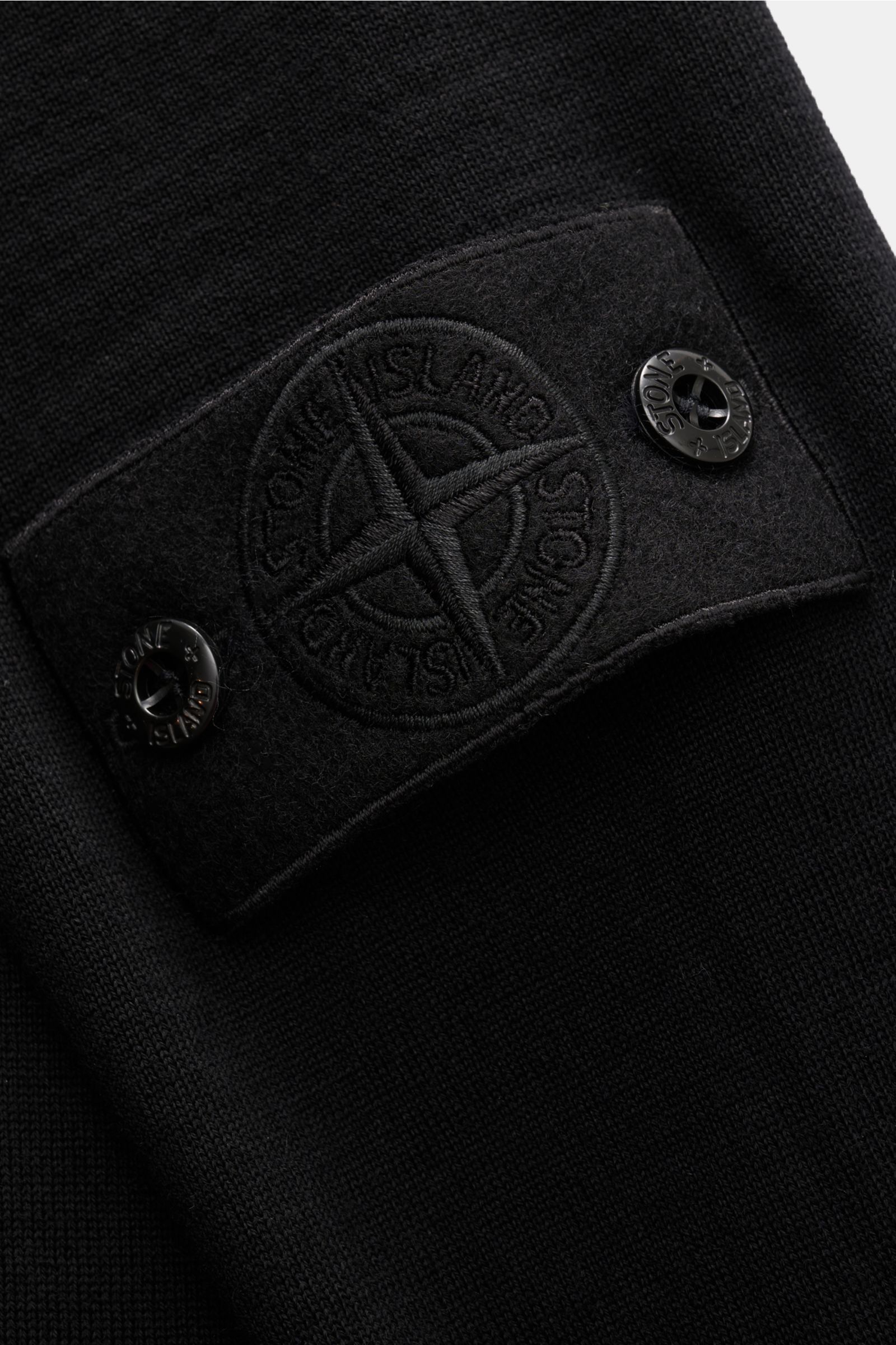 Nahaufnahme des schwarzen Stone Island Strickpolo 'Ghost Pure Light Wool' mit feinem Strickbild, Kompass-Badge am Oberarm und weichem Griff.