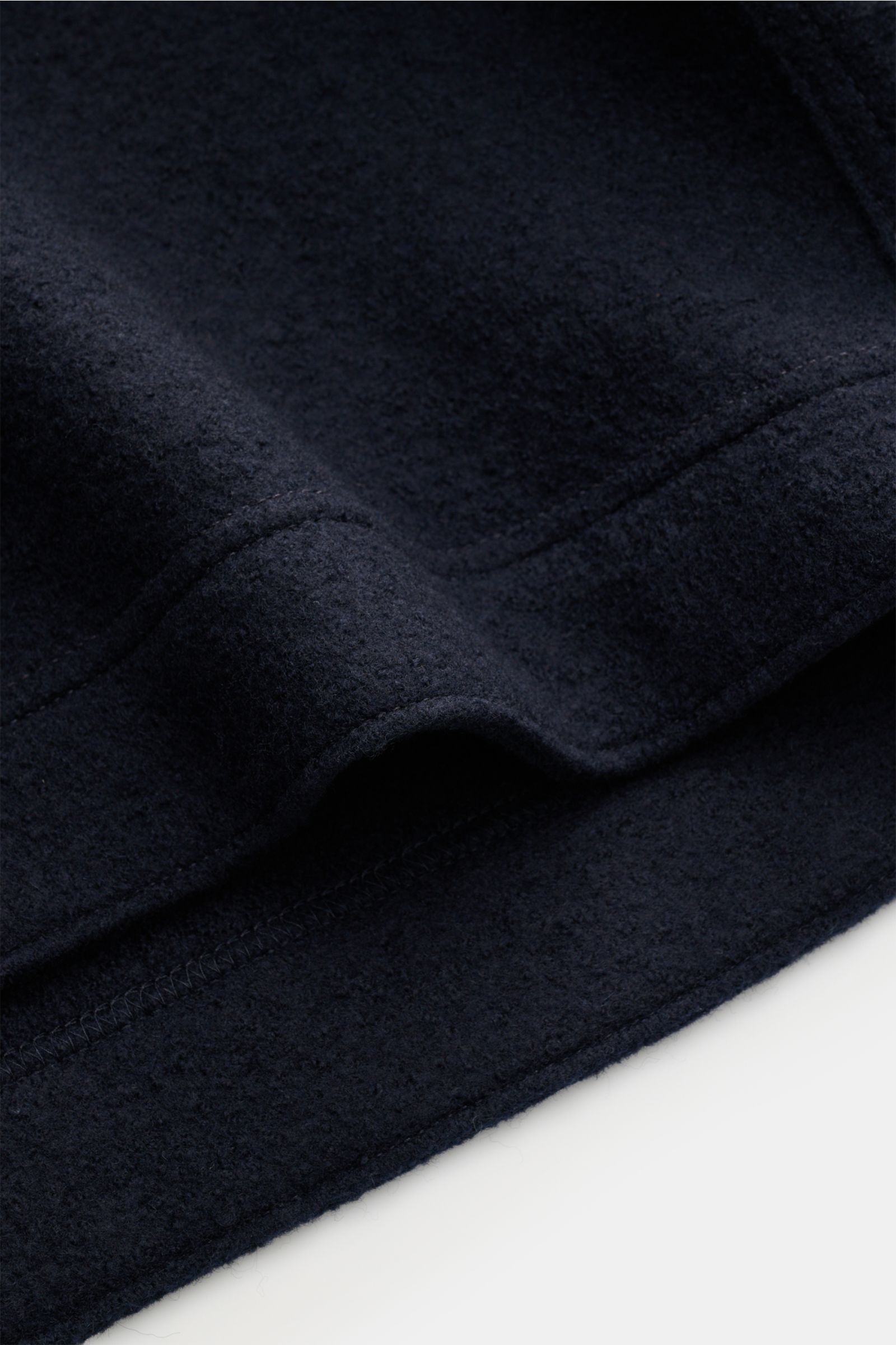 Close-up image of the Stone Island Overshirt navy fabric, photographed from a side angle, showing reine, gefilzte Wolle, weicher Griff, garment dyed, Regular Fit, Druckknopfleiste, Umlegekragen, aufgesetzte Brusttaschen, and typisches Kompass-Badge am Ärm
