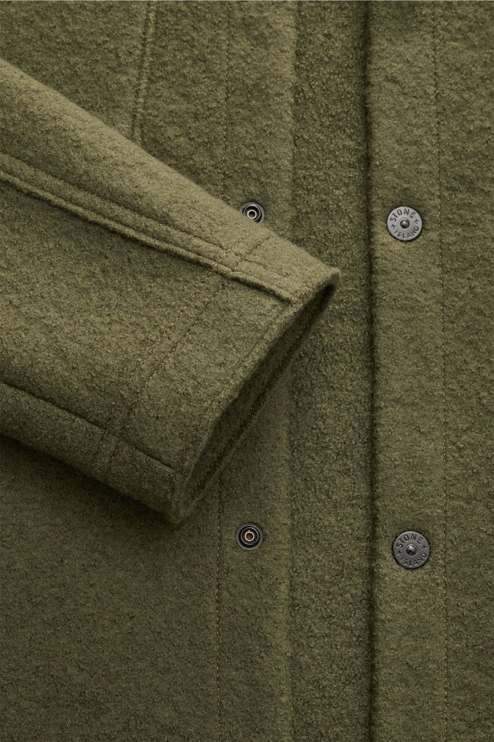 Nahaufnahme eines Stone Island Overshirt oliv aus reiner, gefilzter Wolle mit weichem Griff, garment dyed, Regular Fit, Druckknopfleiste, Umlegekragen, aufgesetzten Brusttaschen und Kompass-Badge am Ärmel.