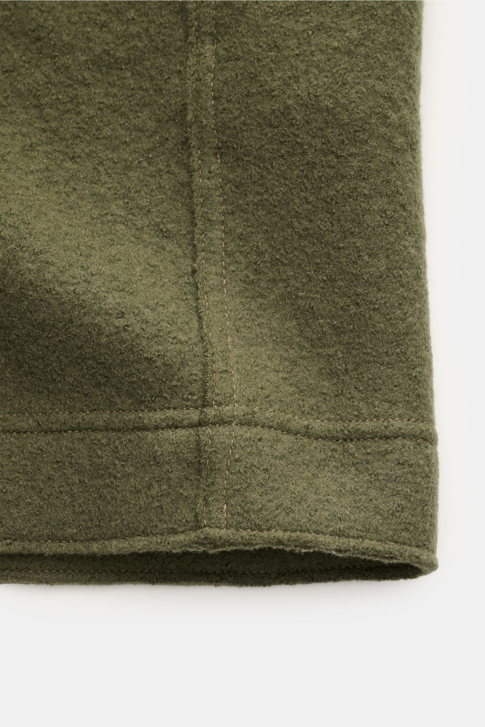 Nahaufnahme des Saums eines Stone Island Overshirt oliv aus reiner, gefilzter Wolle mit weichem Griff, garment dyed, Regular Fit, Druckknopfleiste, Umlegekragen, aufgesetzten Brusttaschen und typischem Kompass-Badge am Ärmel, seitliche Perspektive.