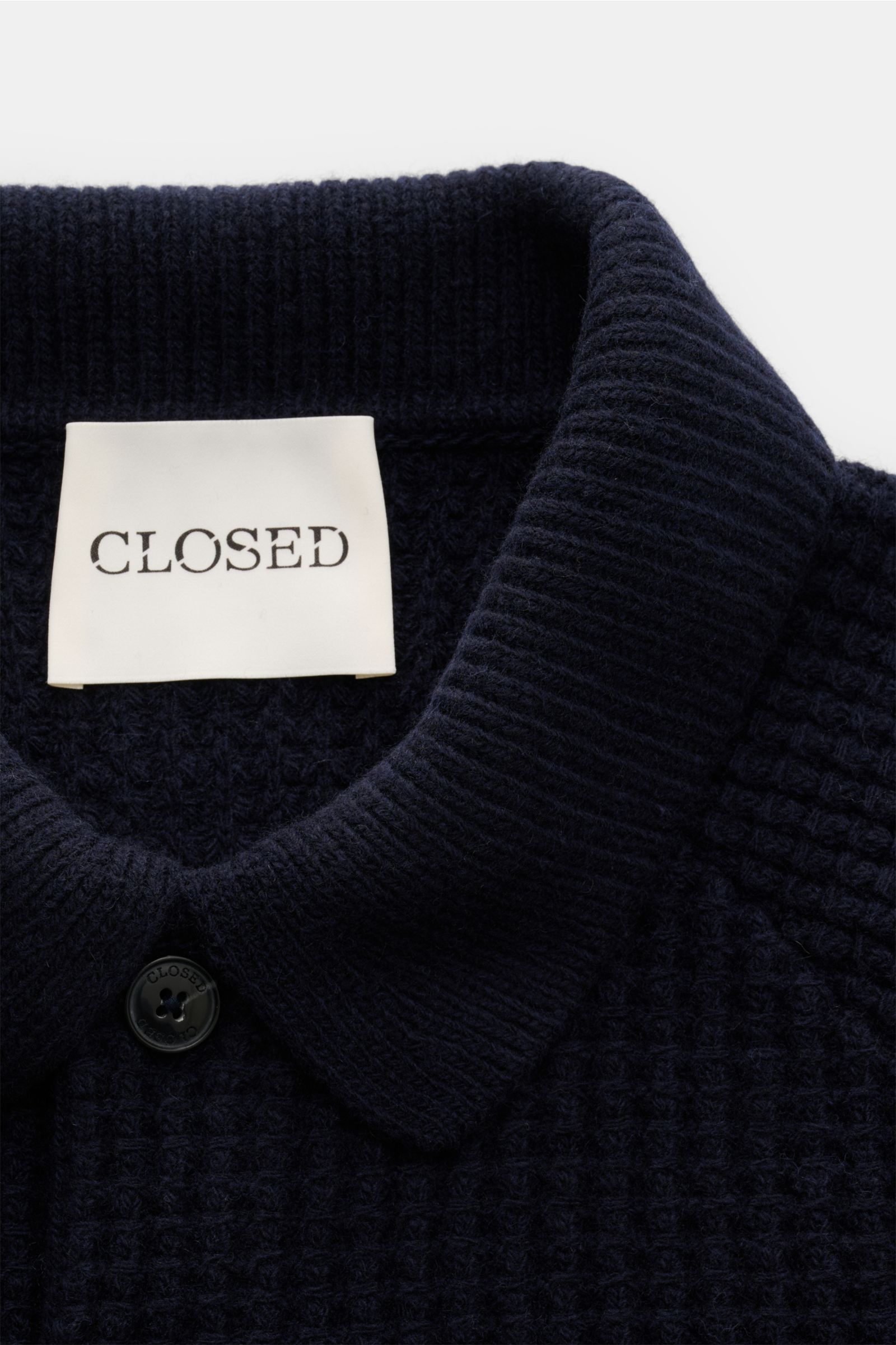 Closed Strickpolo navy shown from a close-up top-down view, featuring a typical polo collar, three-button placket, and waffle knit texture in pure wool with a slim fit and ribbed cuffs; a sporty, warm knit polo with gripping, voluminous quality.
