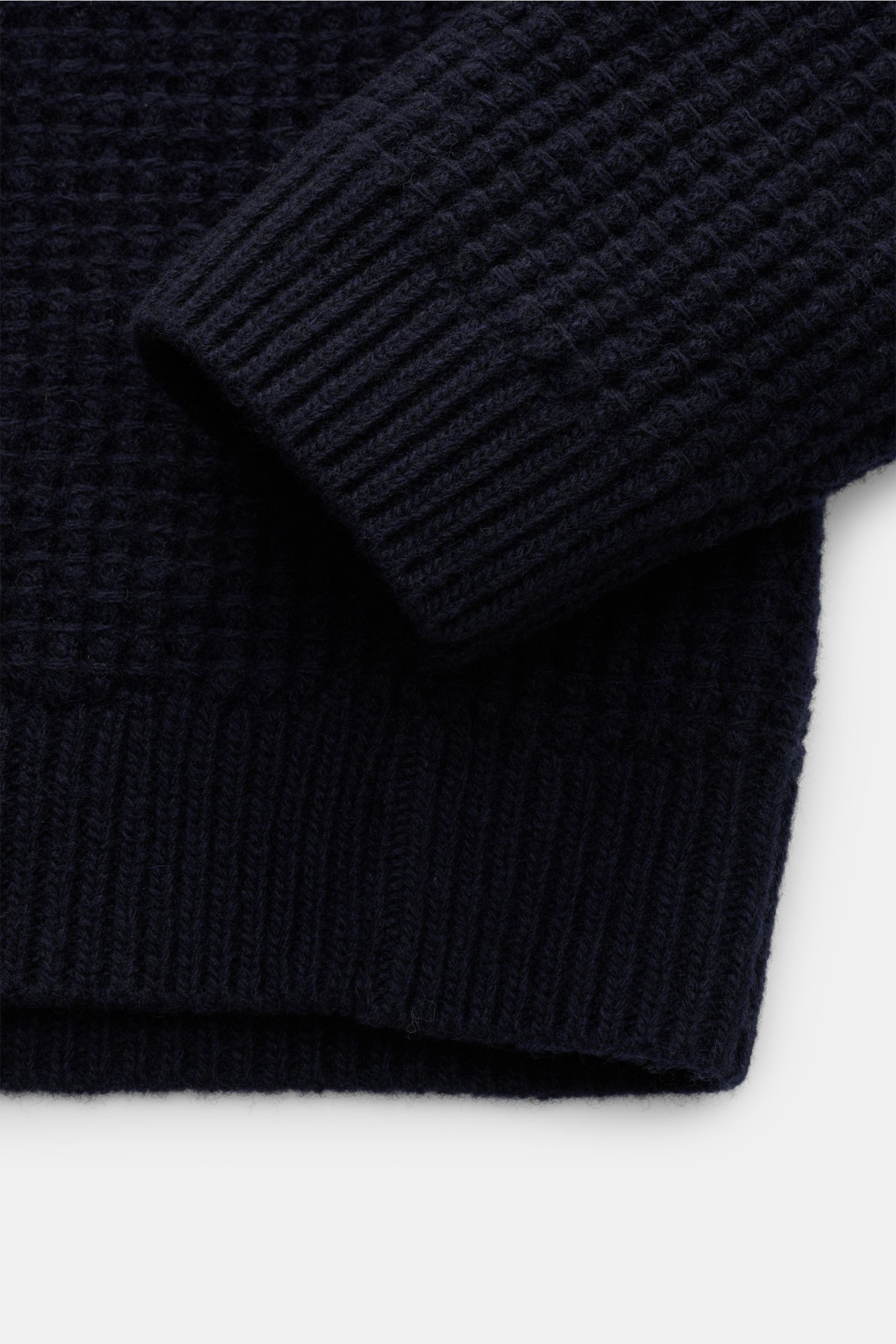 Close-up image of the sleeve and hem of the Closed Strickpolo navy, photographed from a top-down perspective. The slim fit polo features grobes Waffelstrick knit in pure wool, a typical polo collar, a three-button placket, and comfortable ribbed cuffs and