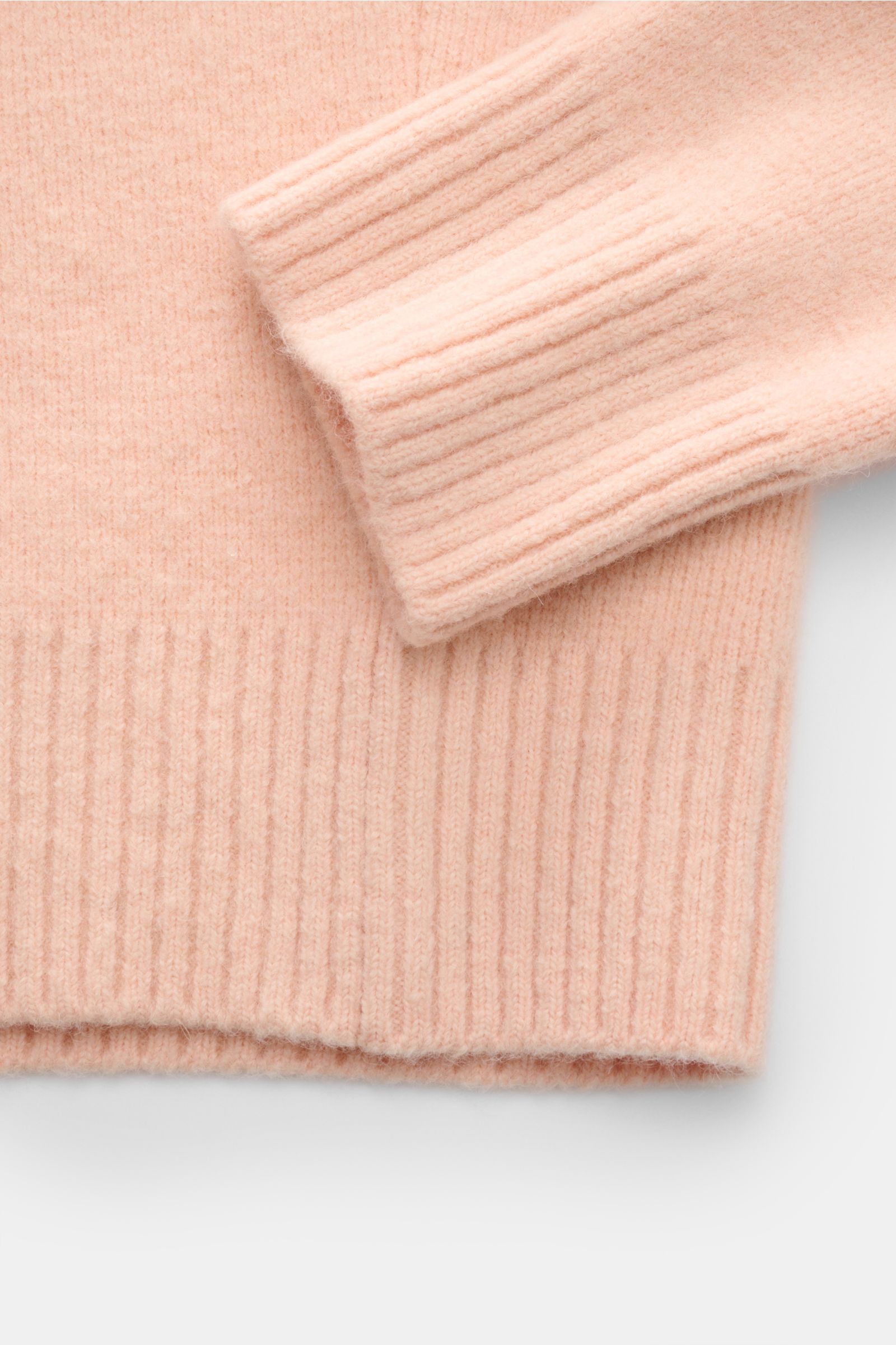 Nahaufnahme des Ami Paris Strickpolo rosé mit elastischem, voluminösem Alpaka-Wollstrick, Rippbündchen und weichem Griff, seitlich fotografiert.