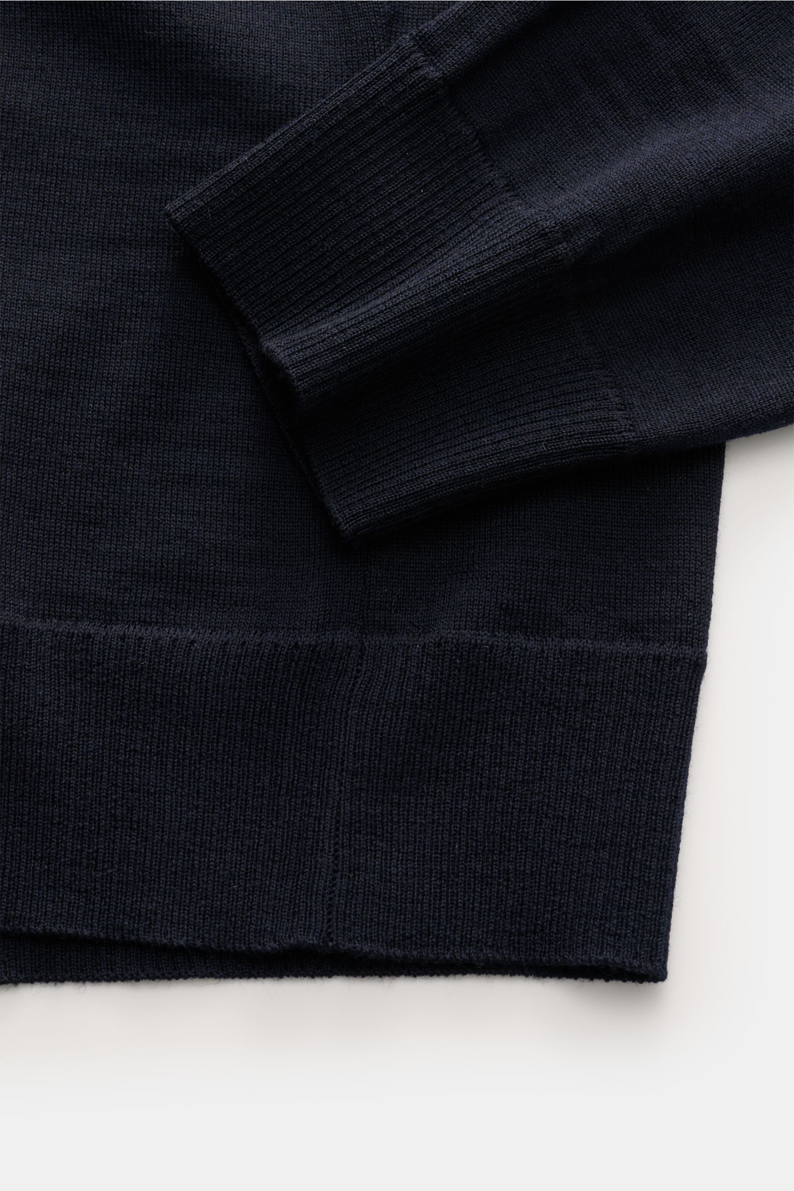 Stone Island Strickpolo 'Ghost Piece' navy aus reiner Schurwolle, weicher Griff, feines Strickbild, Rippbündchen, Detailaufnahme von Ärmel und Saum.