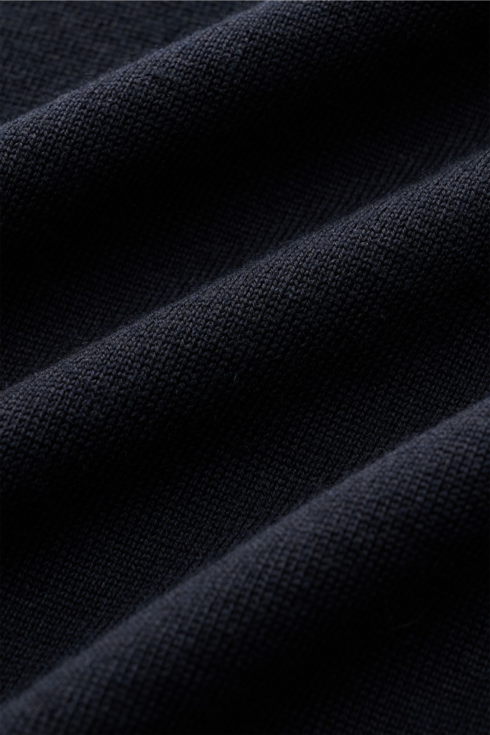 Nahaufnahme des navyfarbenen Stone Island Strickpolo 'Ghost Piece' aus reiner Schurwolle, weicher Griff, feines Strickbild, tonales Kompass-Badge sichtbar.