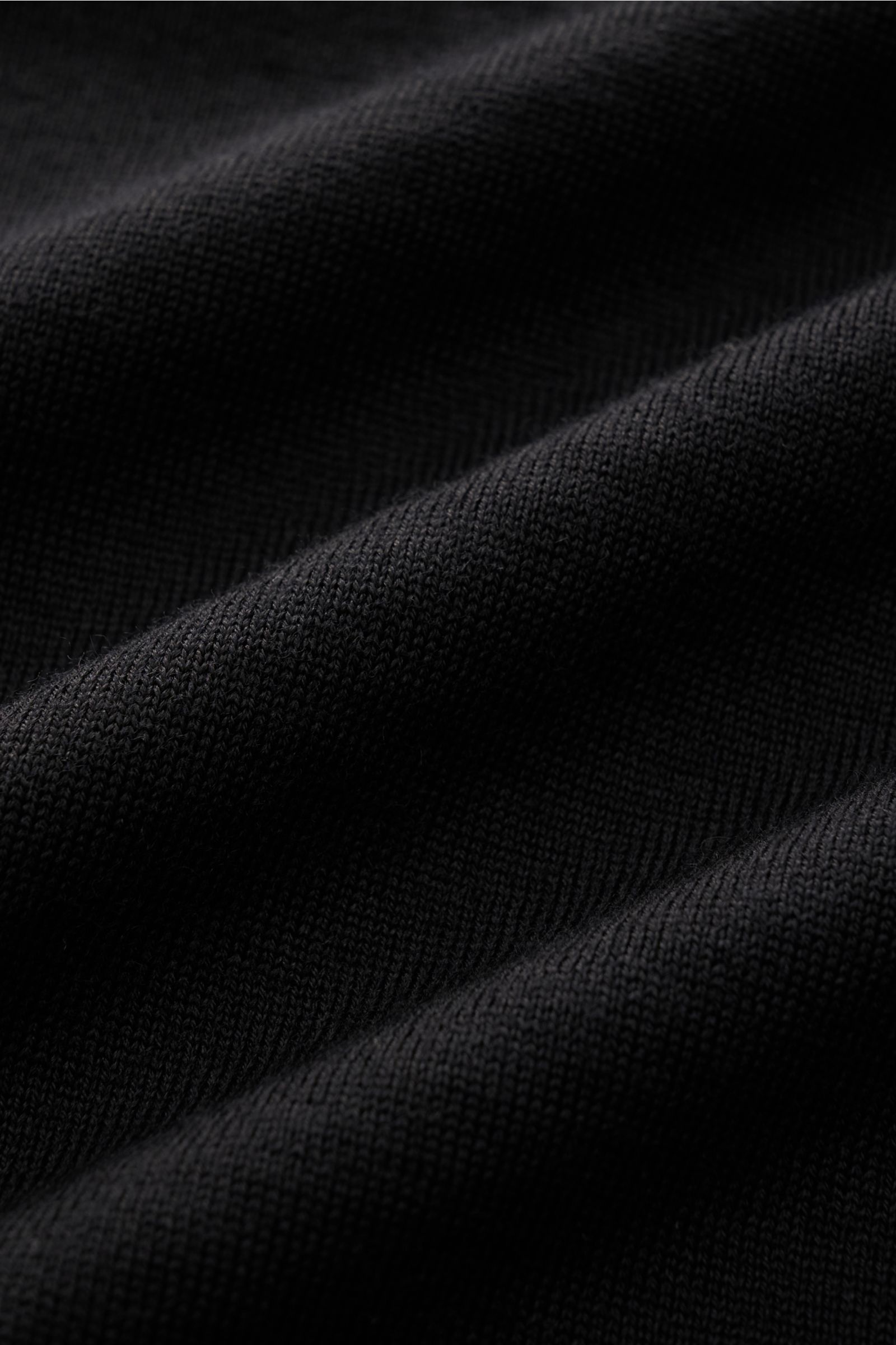 Nahaufnahme der feinen Strickstruktur des Stone Island Strickpolo 'Ghost Pure Light Wool' schwarz mit weichem Griff und Regular Fit.