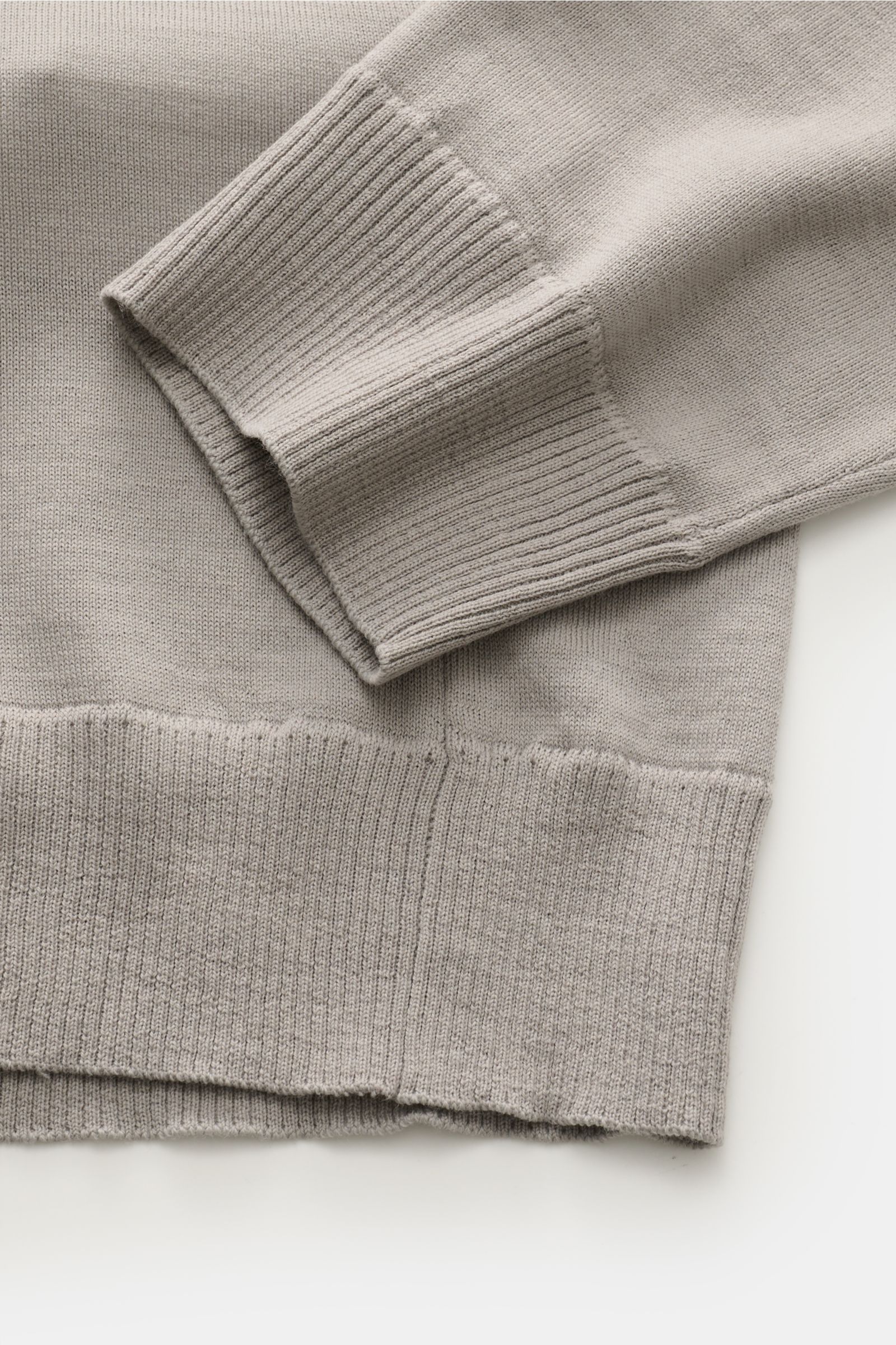 Nahaufnahme des Stone Island Strickpolo 'Ghost Piece' grau von unten rechts, zeigt weiche Schurwolle, feines Strickbild, Rippbündchen und tonales Kompass-Badge.