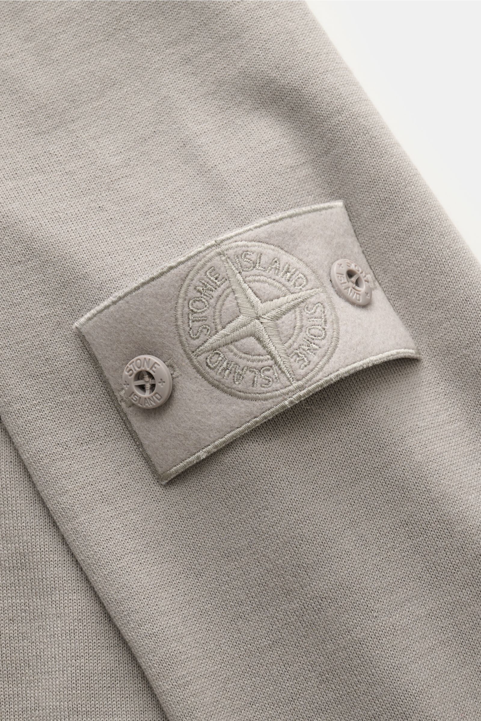 Stone Island Strickpolo 'Ghost Piece' grau aus reiner Schurwolle, weiches, feines Strickbild, tonales Kompass-Badge am Ärmel, Nahaufnahme.