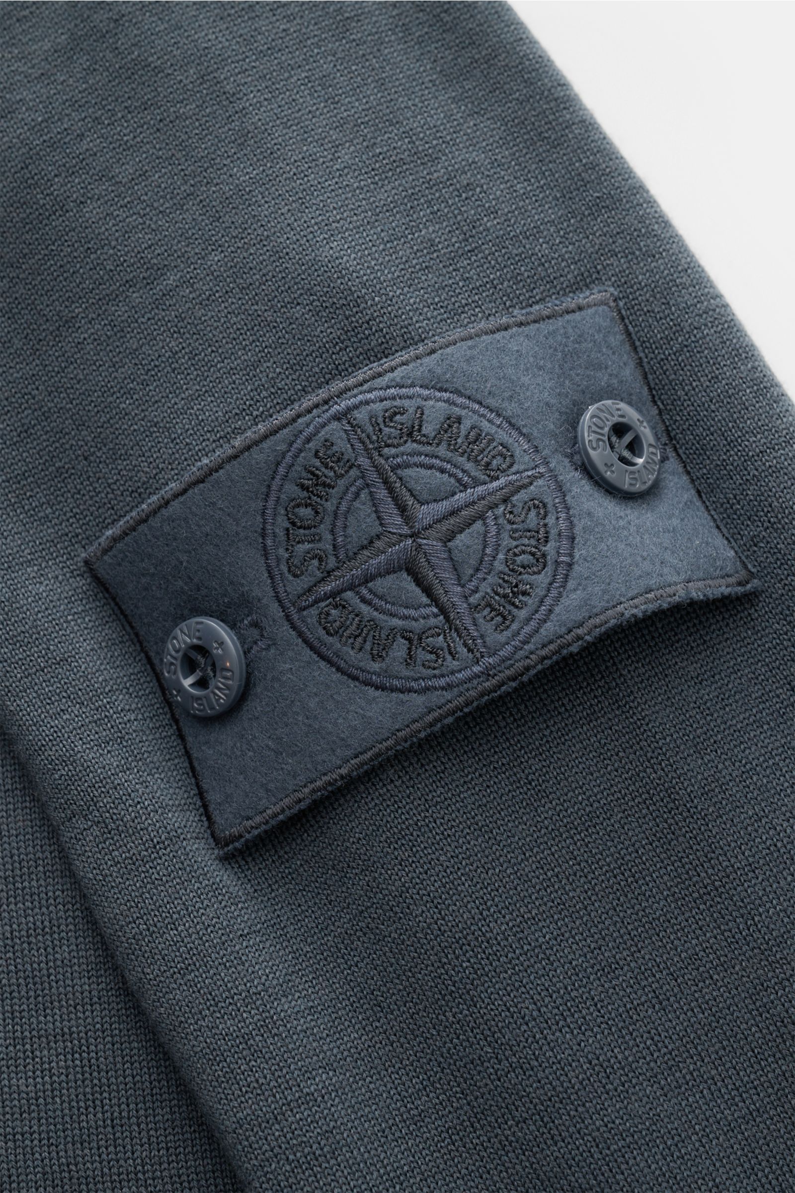 Stone Island Strickpolo 'Ghost Piece' dunkelgrau, Nahaufnahme von Ärmel mit tonalem Kompass-Badge aus weicher reiner Schurwolle.