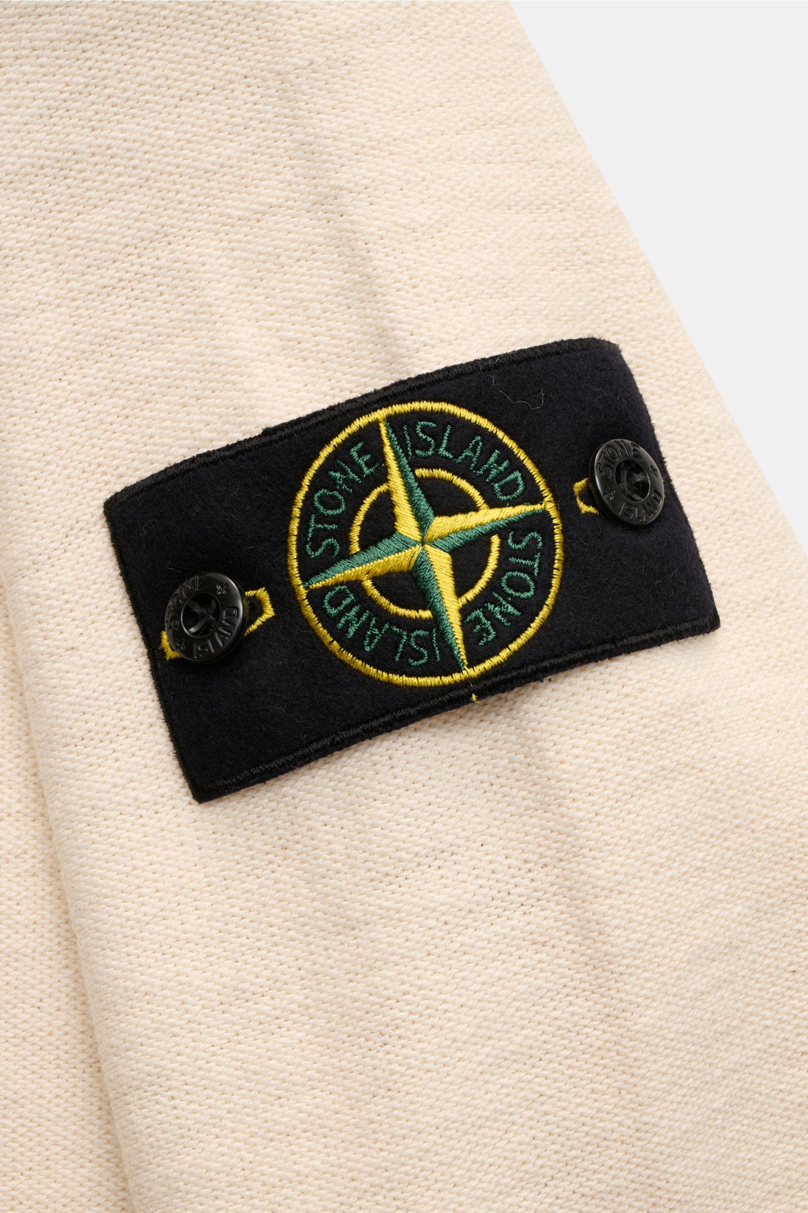 Close-up side view of the Stone Island Half-zip jumper cream, showing the signature compass badge on the sleeve, knitted in a modern purl stitch with a blend of cotton and microfibre, slightly robust to the touch with medium-fine knit, slim fit, standing 
