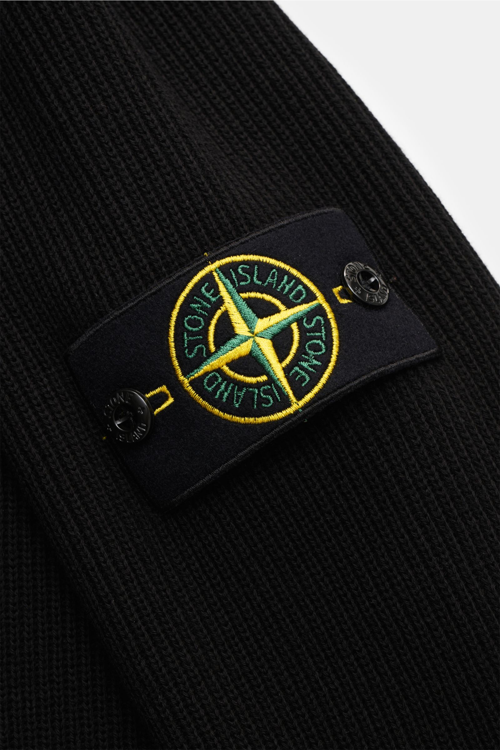Nahaufnahme des schwarzen Stone Island Troyer mit markentypischem Kompass-Badge am eingestrickten Raglanärmel, Strick aus reiner Baumwolle, mittelfeines Strickbild, Slim Fit, Rippstrickkragen mit Zipper und Rippstrickbündchen, leicht griffige Haptik, seit