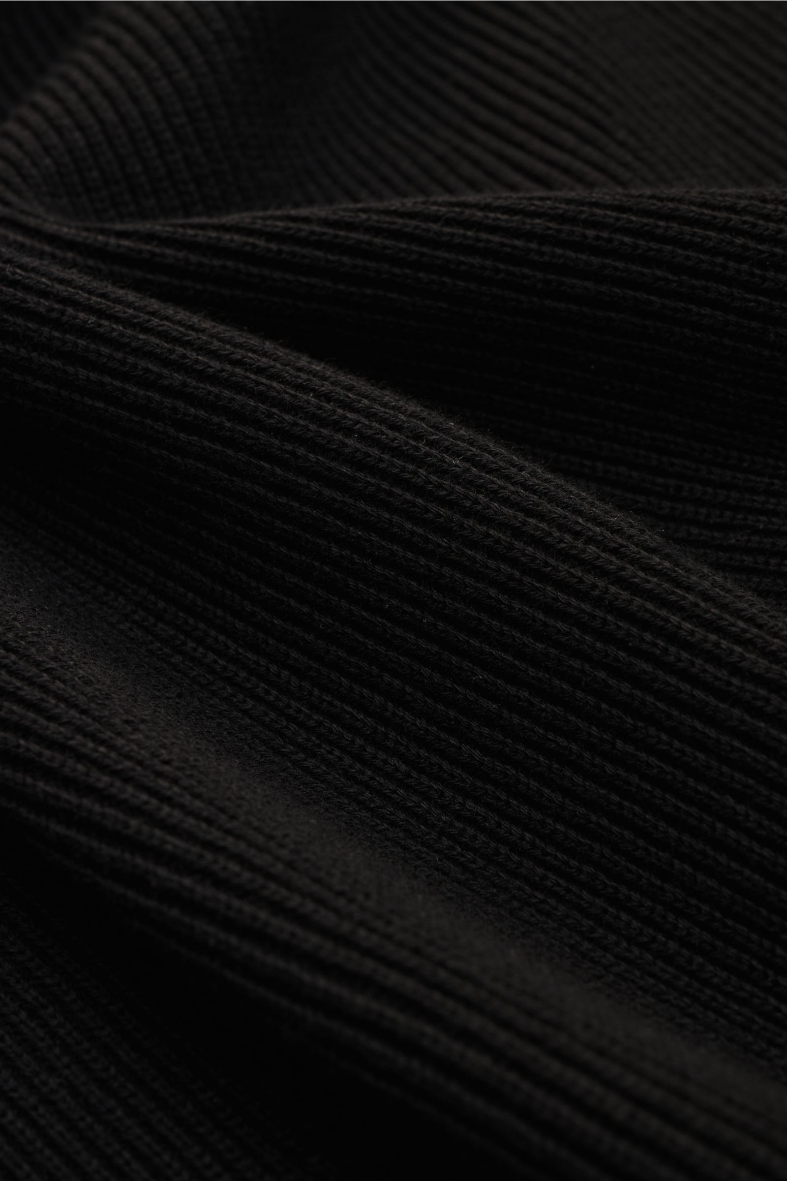 Nahaufnahme des schwarzen Stone Island Troyer aus mittelfeinem, reiner Baumwolle Strick mit leicht griffiger Haptik, Slim Fit, Rippstrickkragen mit Zipper, eingestricktem Raglanärmel, markentypischem Kompass-Badge am Oberarm und Rippstrickbündchen, fotogr