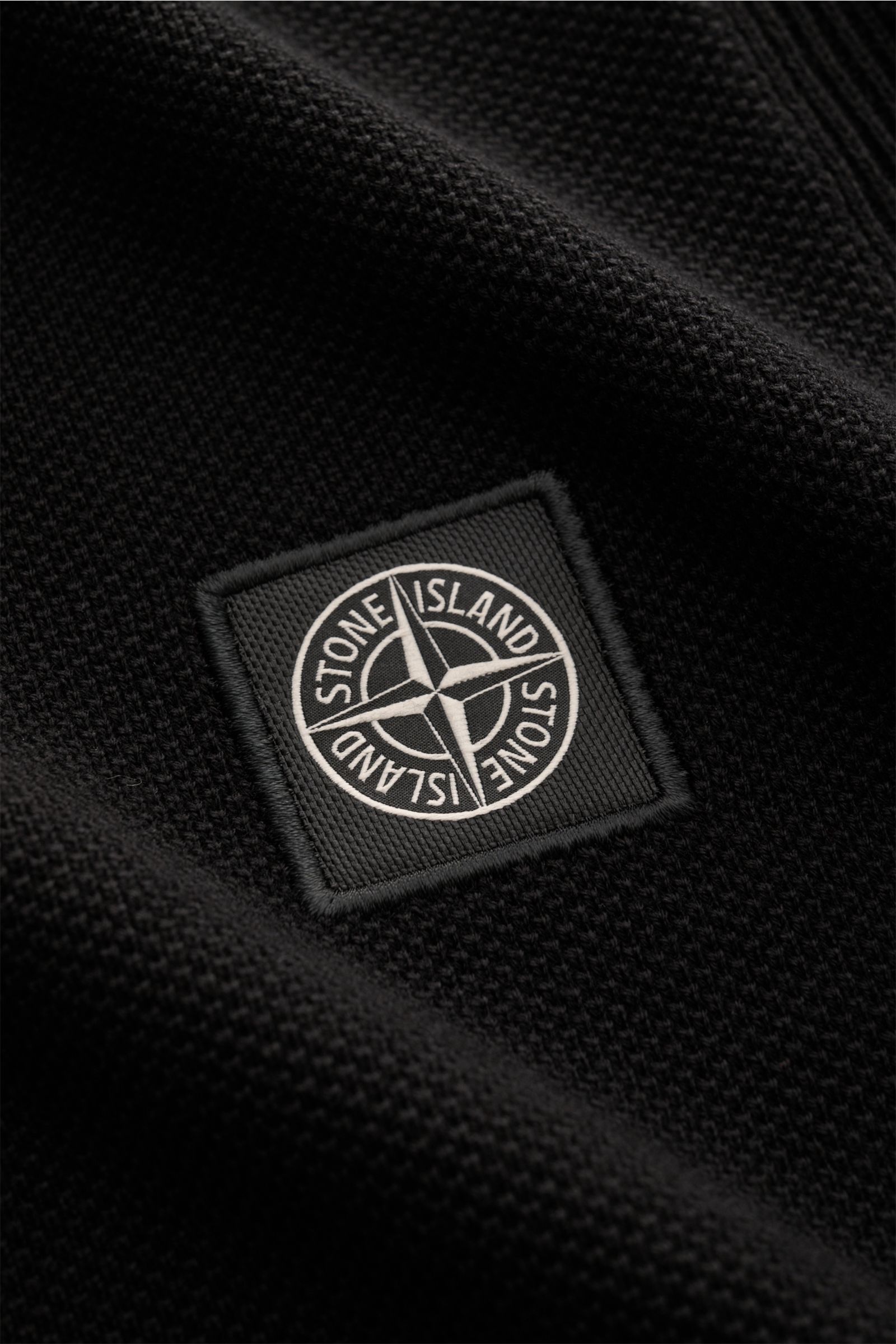 Nahaufnahme des Stone Island Kurzarm-Strickpolo schwarz mit feinem Piqué-Mix, Polokragen und STONE ISLAND-Weblabel frontal sichtbar.
