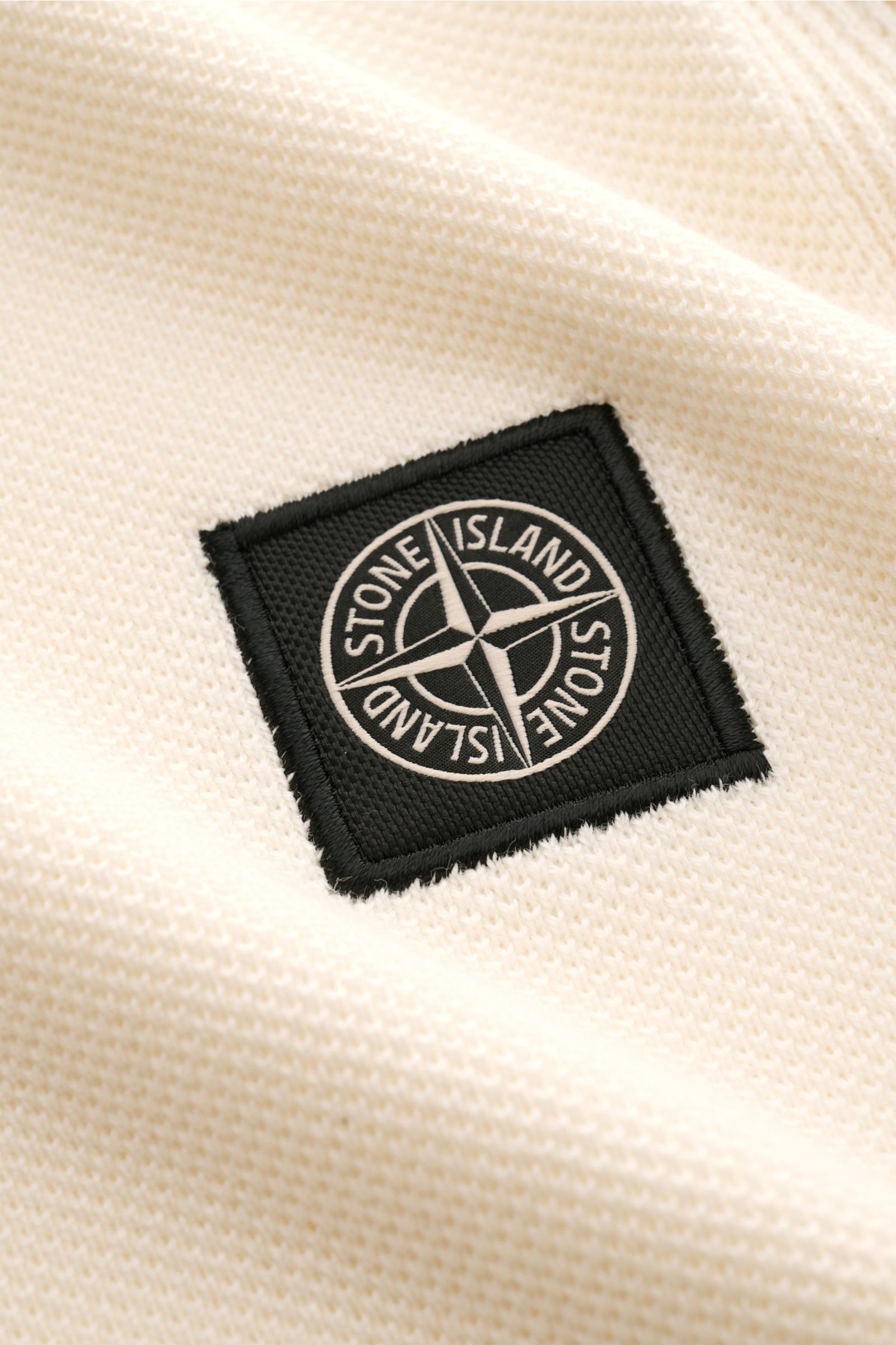 Stone Island Kurzarm-Strickpolo creme in Nahaufnahme von Stoffstruktur und schwarzem Weblabel, reine Baumwolle, feiner Piqué-Mix.