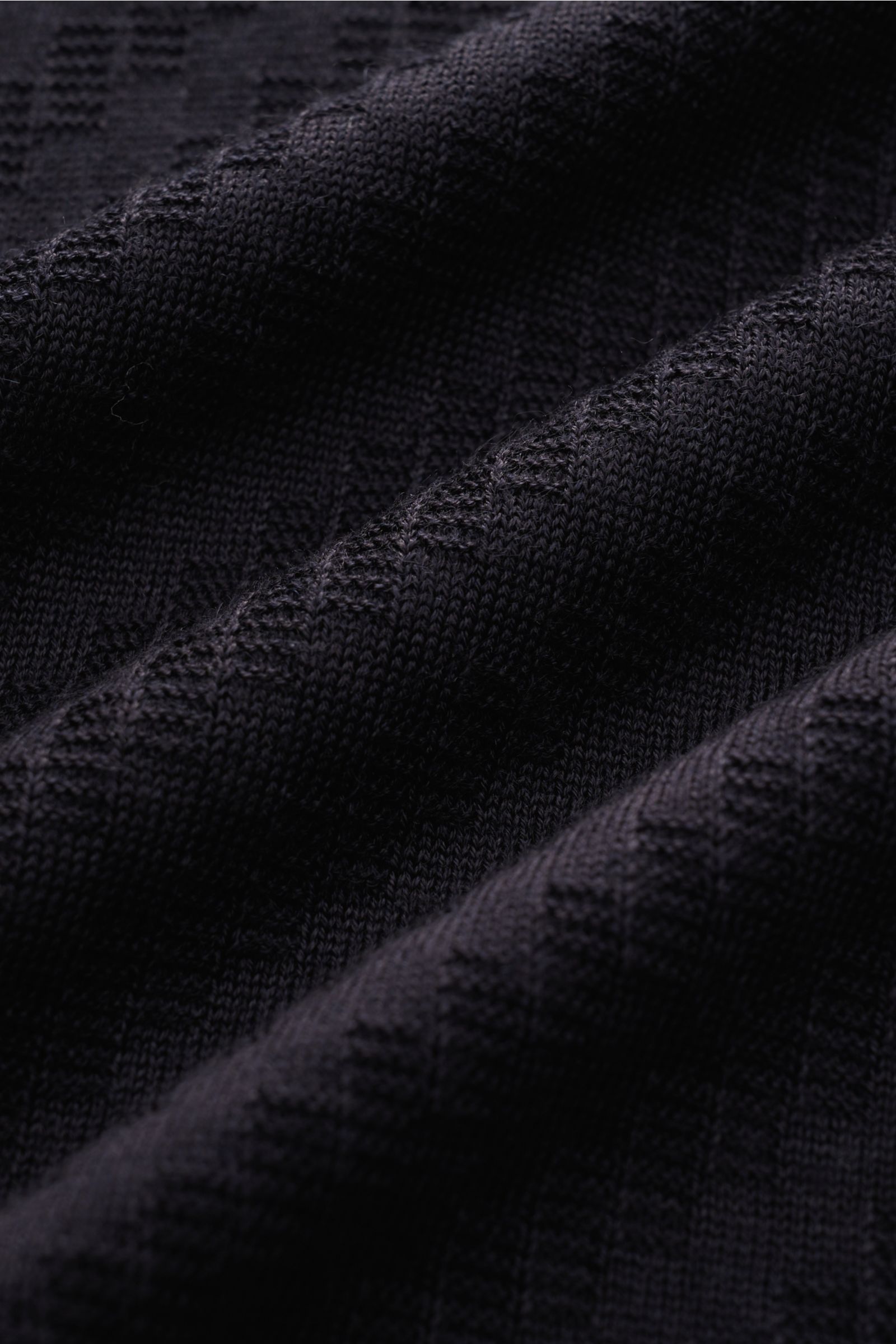 Nahaufnahme eines Emporio Armani Kurzarm-Strickpolo navy mit feinem Strukturstrick und weichem Griff, fotografiert aus schräger Perspektive.