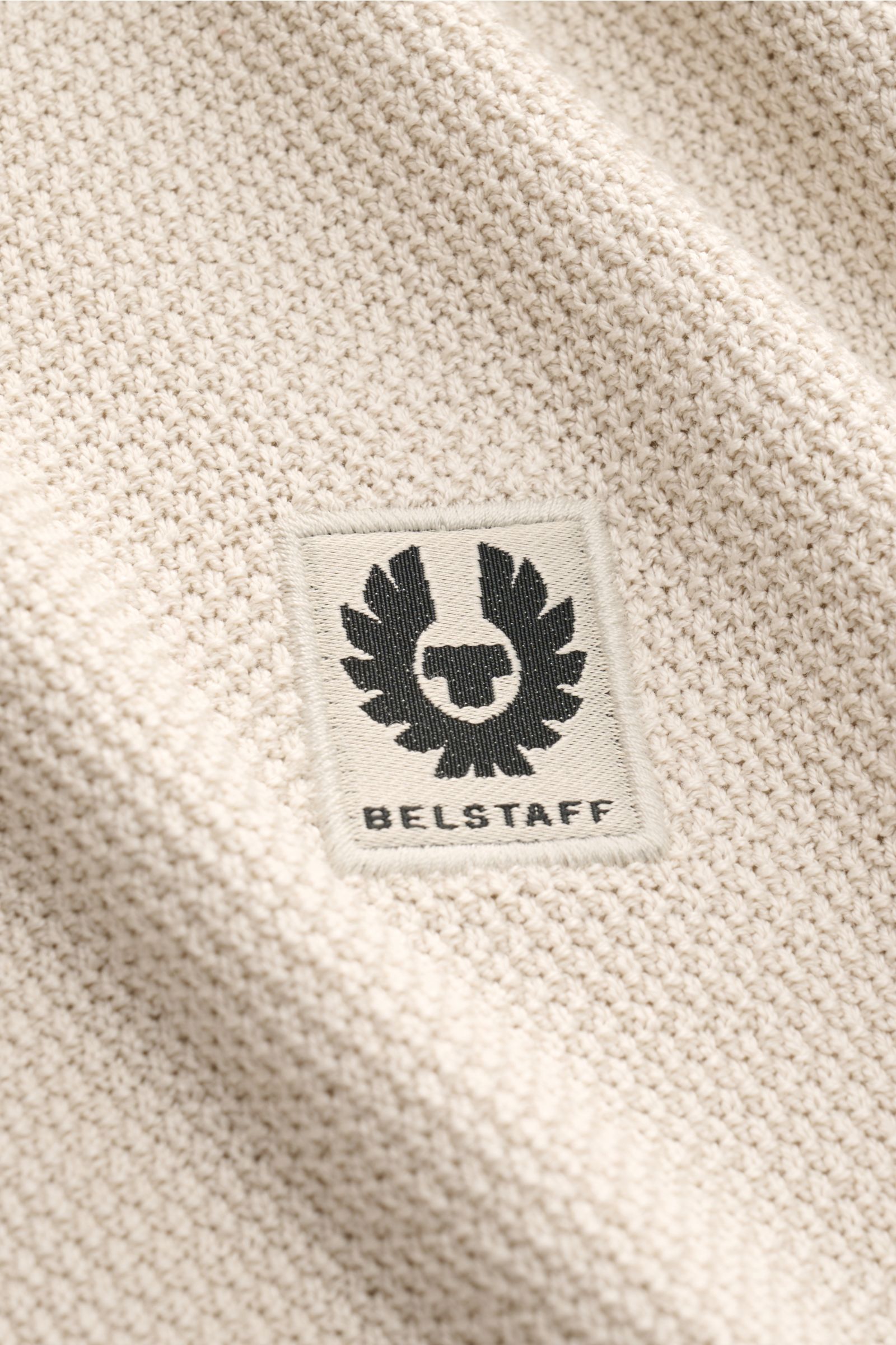 Nahaufnahme des Weblabels auf dem Oberarm des beigefarbenen Belstaff Kurzarm-Strickpolo 'Coast' mit feinem Strukturstrick und weichem Griff.
