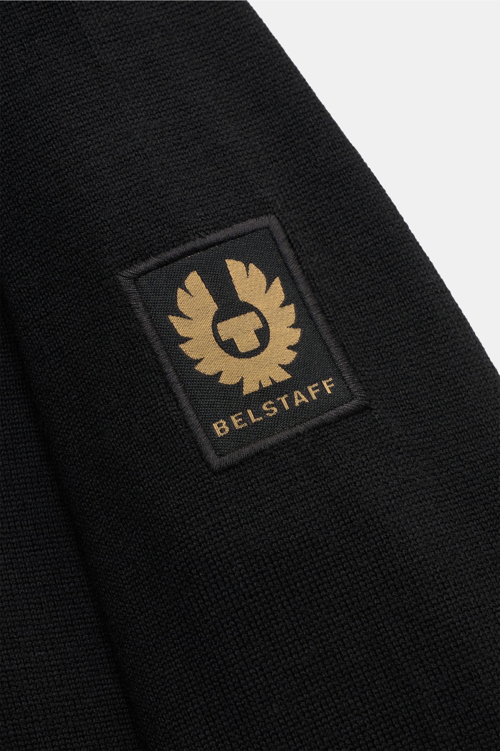 Alt-Tag (124 Zeichen): Nahaufnahme des Weblabels am Oberarm des Belstaff Strickpolo 'Kyle' schwarz aus reiner Wolle mit feinem Strickbild.