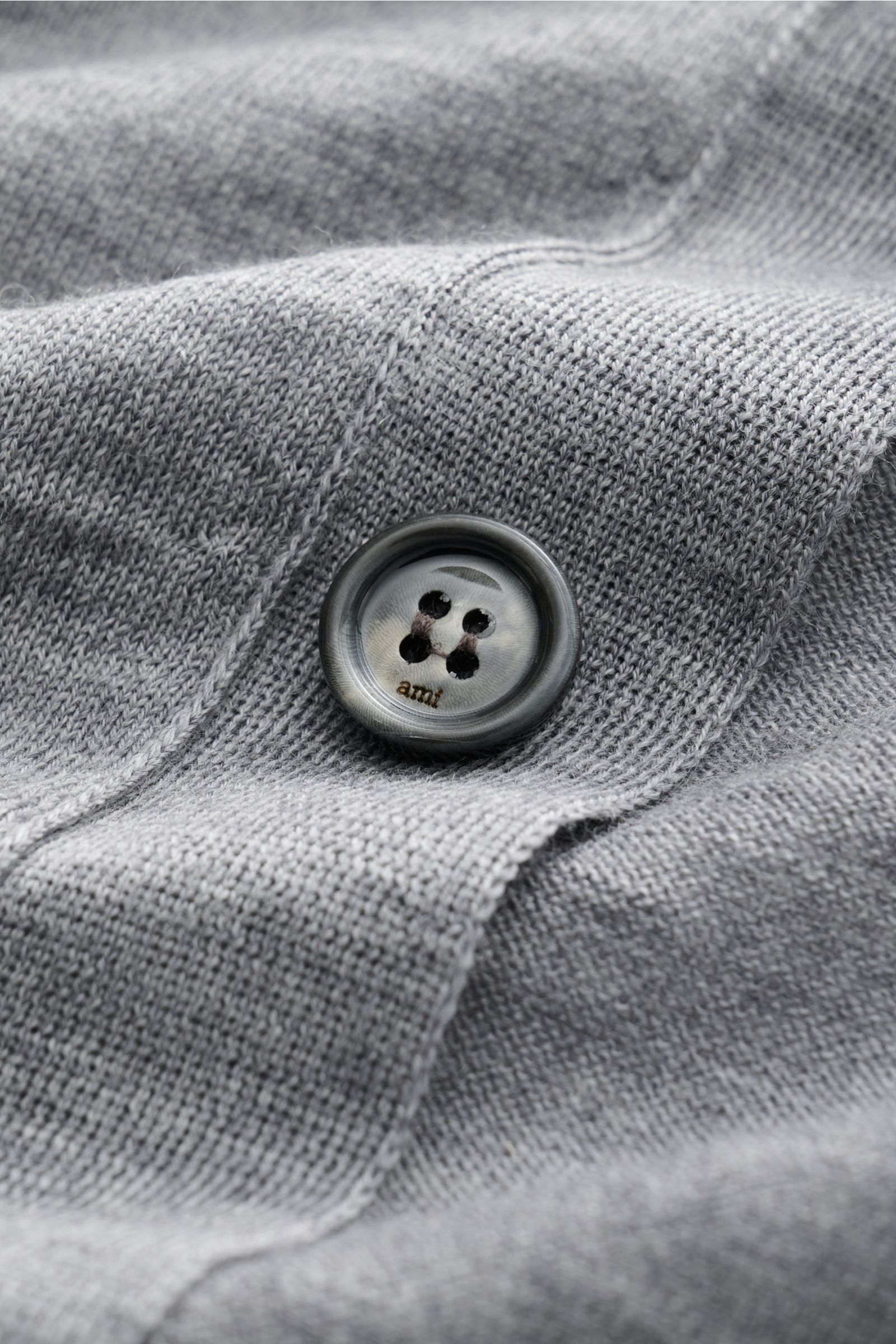 Nahaufnahme des Ami Paris Merino Cardigan grau meliert mit gestricktem Umlegekragen, sechs Knöpfen, Raglanärmel, Logo-Stitching, feinem Strickbild und Rippbündchen aus reiner Merinowolle, weicher Griff, Regular Fit.