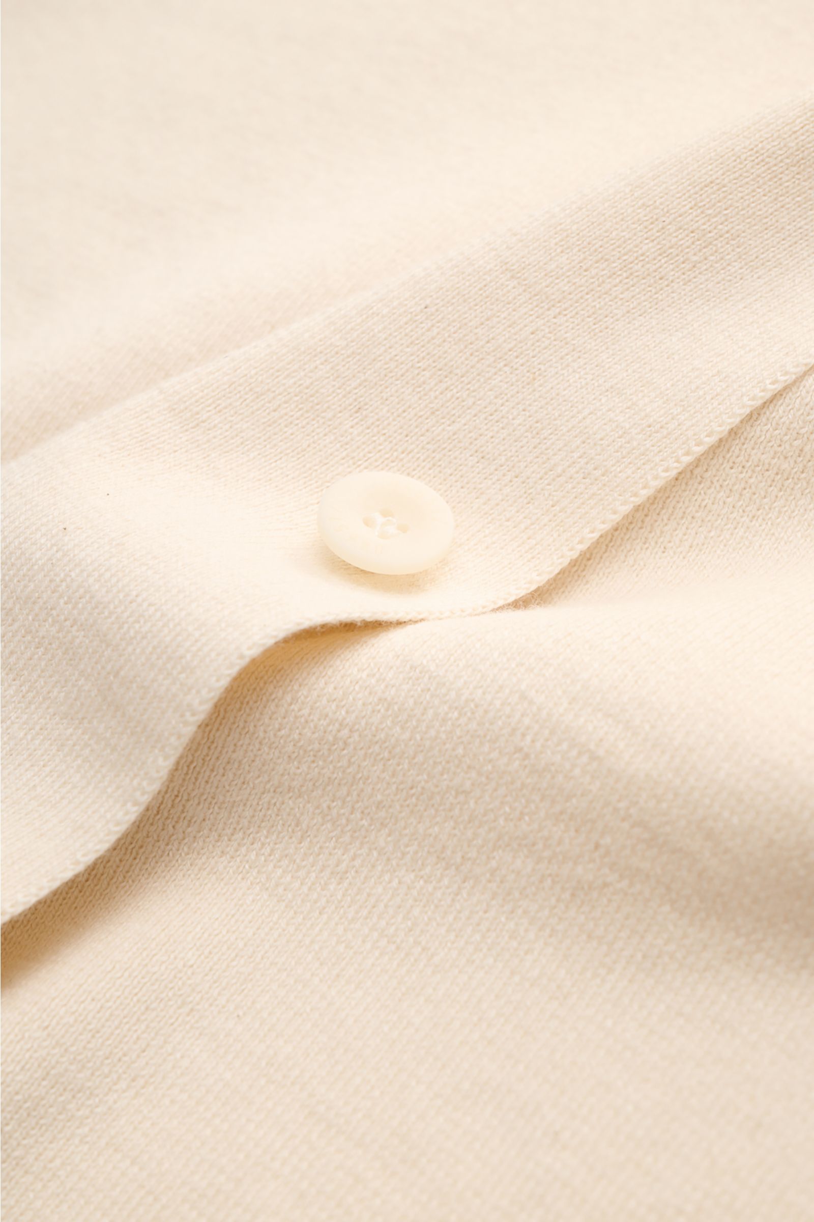 Close-up front view of the cream fabric and button placket of the 04651/ A trip in a bag Short sleeve knit shirt 'Colour Block' cream/black.

An eye-catching piece for summer: This short sleeve knit shirt by 04651/ A TRIP IN A BAG has a distinctive col