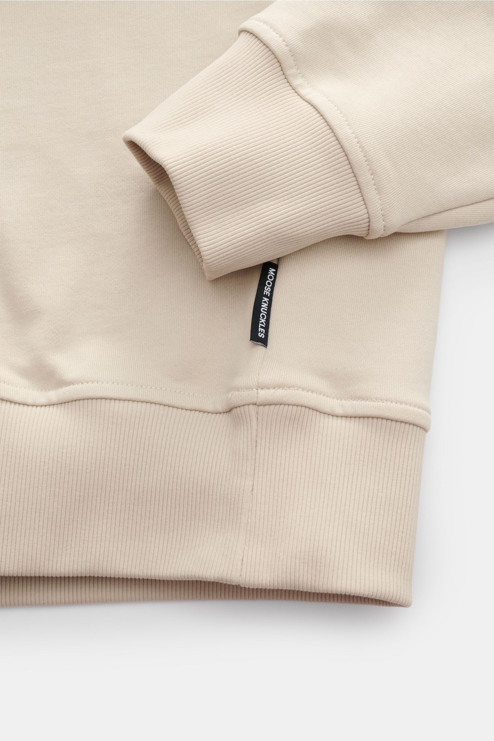 Nahaufnahme von elastischem Rippbündchen und Saum des Moose Knuckles Sweat-Troyer 'Hartsfield' creme aus reiner Baumwolle, weicher Griff, Regular Fit, hoch schließender Kragen mit Zipper, Metall-Logo am Oberarm.