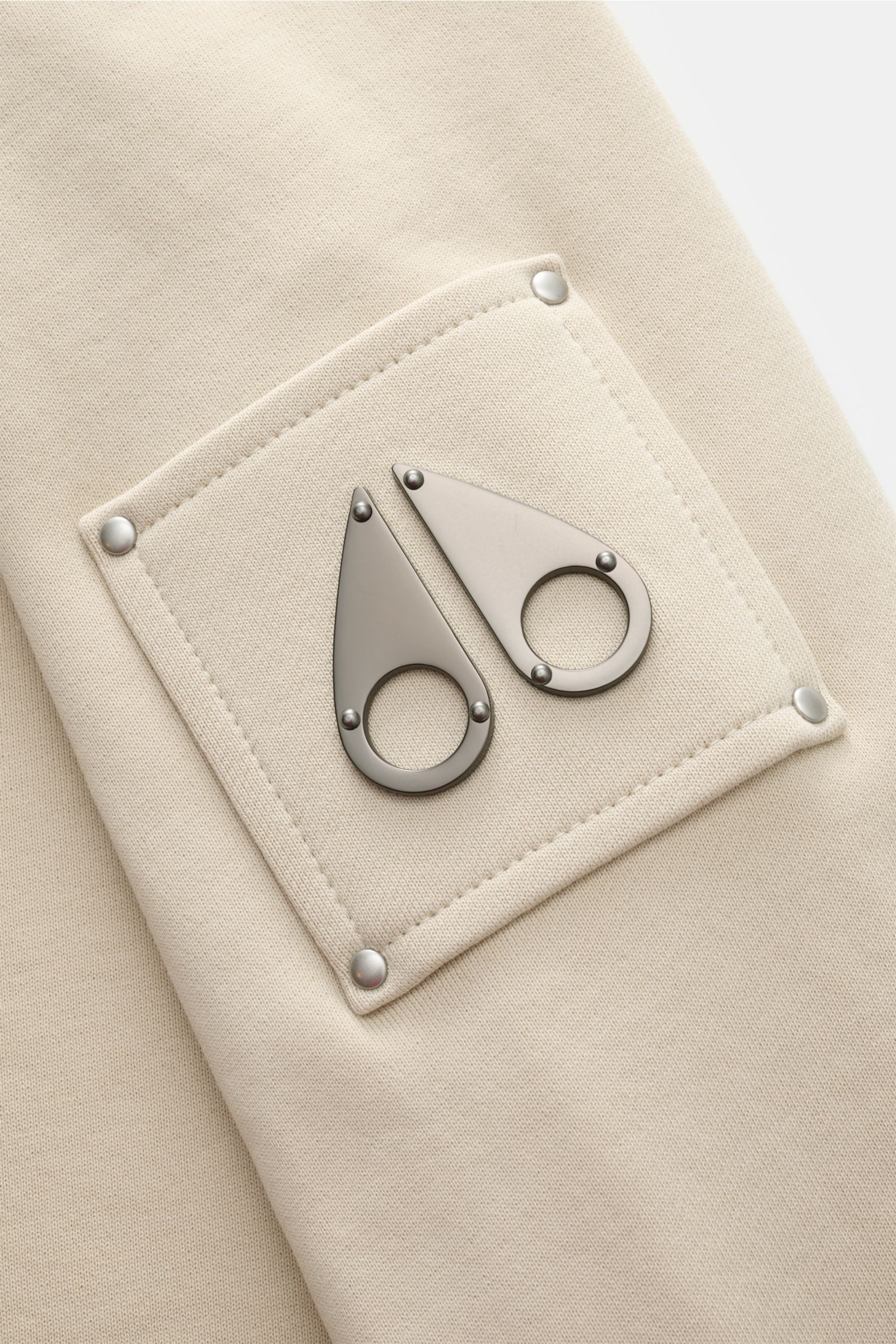 Nahaufnahme des Ärmels vom Moose Knuckles Sweat-Troyer 'Hartsfield' creme, Sweat aus reiner Baumwolle mit weichem Griff, Regular Fit, hoch schließendem Kragen mit Zipper, typischem Metall-Logo am Oberarm und elastischen Rippbündchen.