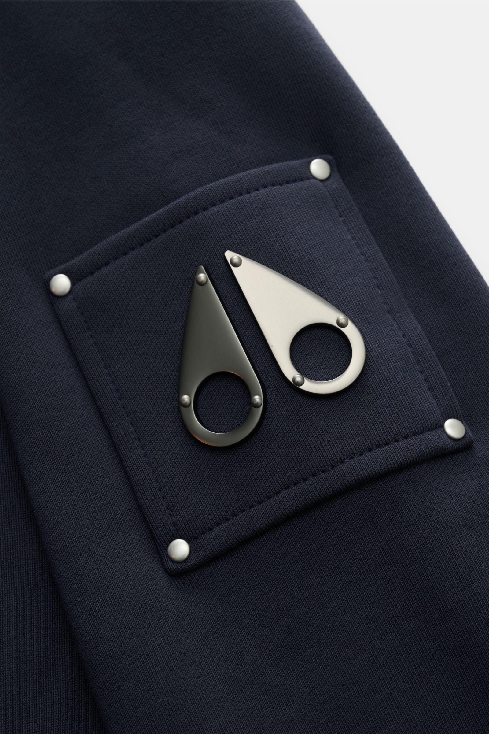 Close-up view of the Moose Knuckles Sweat-Troyer 'Hartsfield' navy showing the metal logo on the upper arm pocket, made of pure cotton with a soft touch, regular fit, high collar with zipper, and elastic rib cuffs. Leger durch den Herbst: Der Sweat-Tro