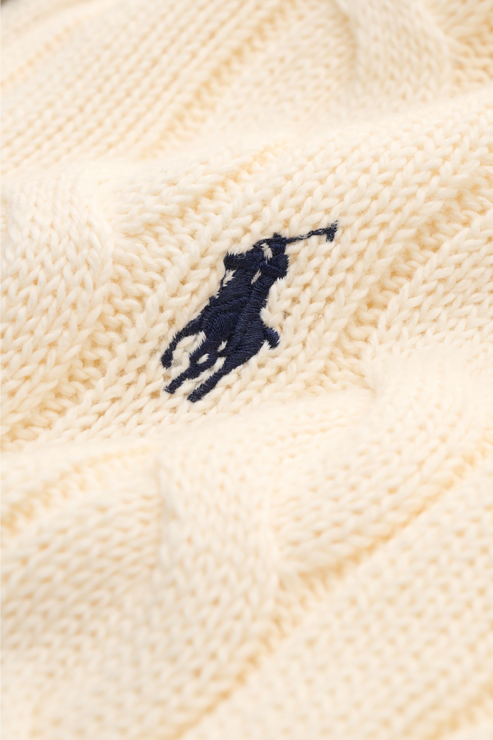 Polo Ralph Lauren Troyer creme in Nahaufnahme, Zopfstrickmuster, weiche Baumwolle, kontrastierendes Polospieler-Stitching frontal sichtbar.