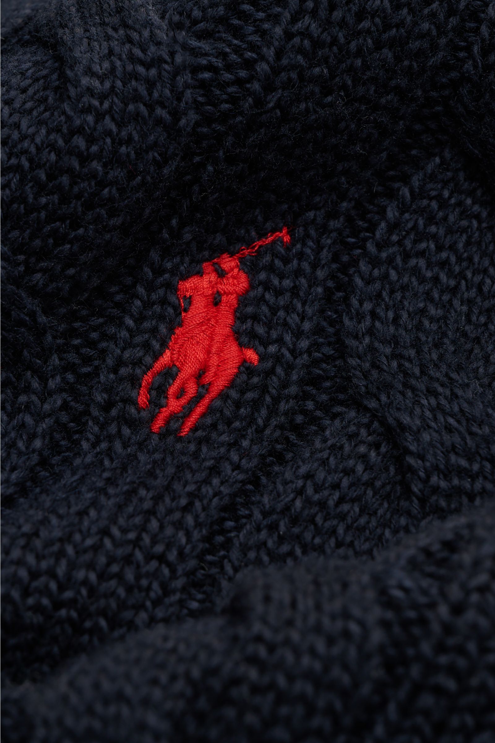 Nahaufnahme des Zopfstrickmusters und roten Polospieler-Stitchings auf der Brust des Polo Ralph Lauren Troyer navy aus reiner Baumwolle.