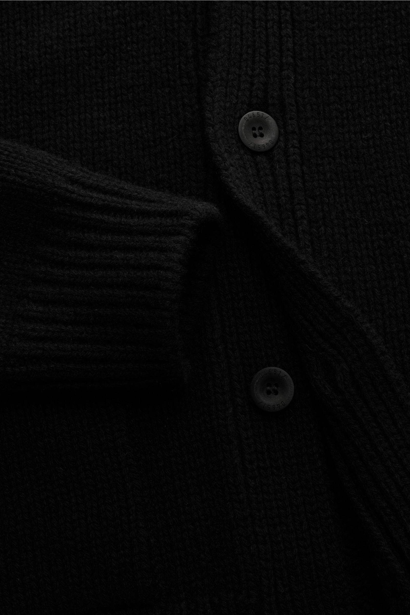 Schwarz fotografierte Detailansicht des 04651/ A trip in a bag Cashmere Cardigan schwarz mit V-Ausschnitt, Slim Fit, vier Knöpfen, grobem Strickbild, reiner Cashmere, weichem Griff, aufgesetzten Hüfttaschen und komfortablen Rippbündchen.