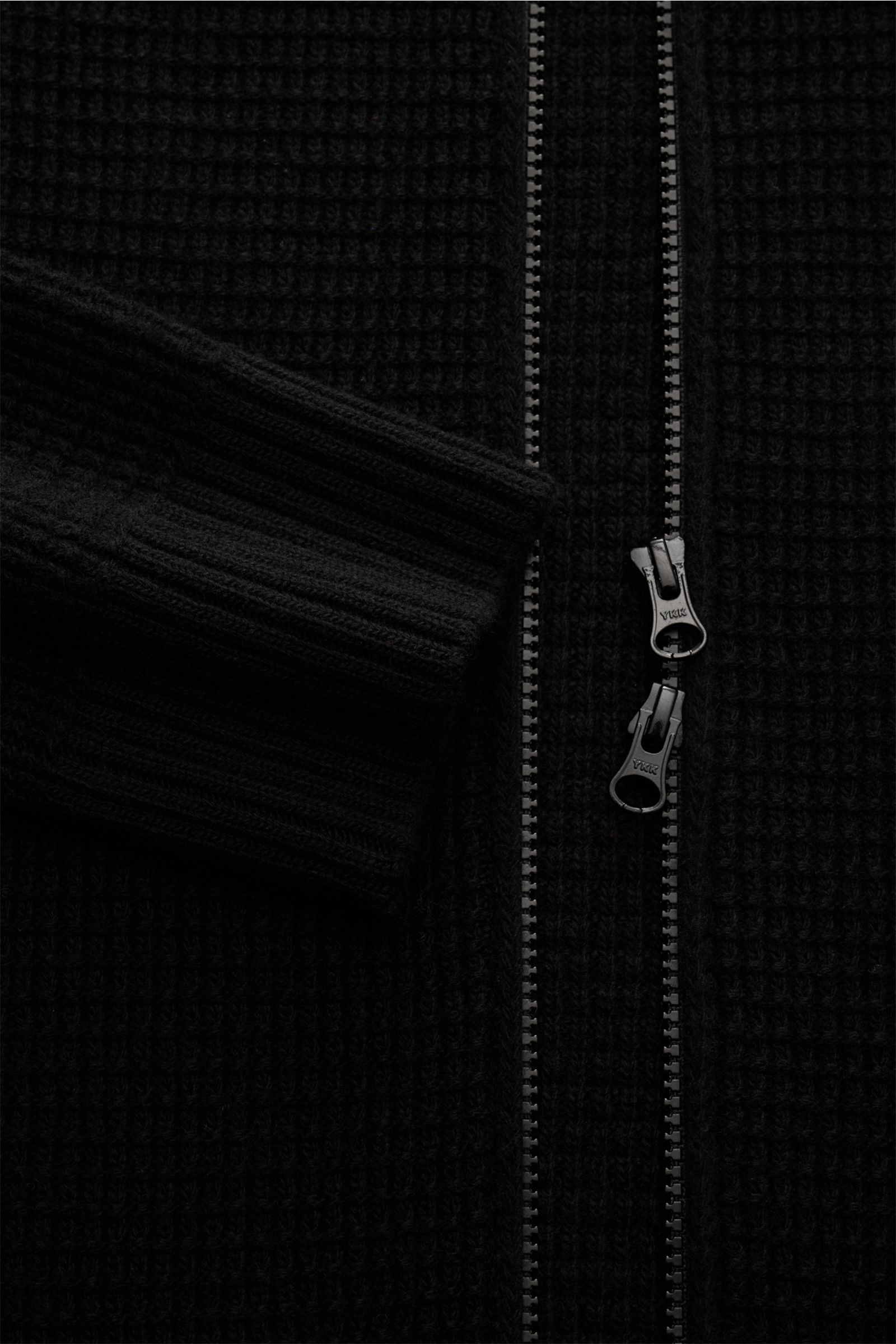 Close-up front view of the Stone Island Strickjacke 'Ghost Piece' schwarz, showing its textured black knit, double zipper, and ribbed cuff. Vielseitiges Winter-Essential: Die Strickjacke aus der Ghost-Kollektion von STONE ISLAND bietet zahlreiche Kombi
