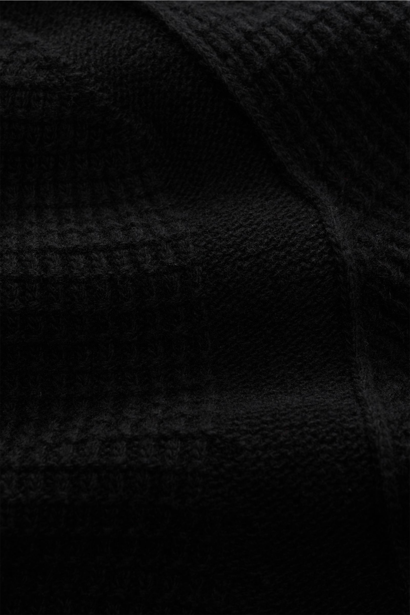 Close-up front view of Stone Island Strickjacke 'Ghost Piece' schwarz showing its textured black wool knit with tonal compass badge, versatile winter essential with pure wool, structured grip, medium-fine knit, regular fit, high collar, two-way zipper, ra