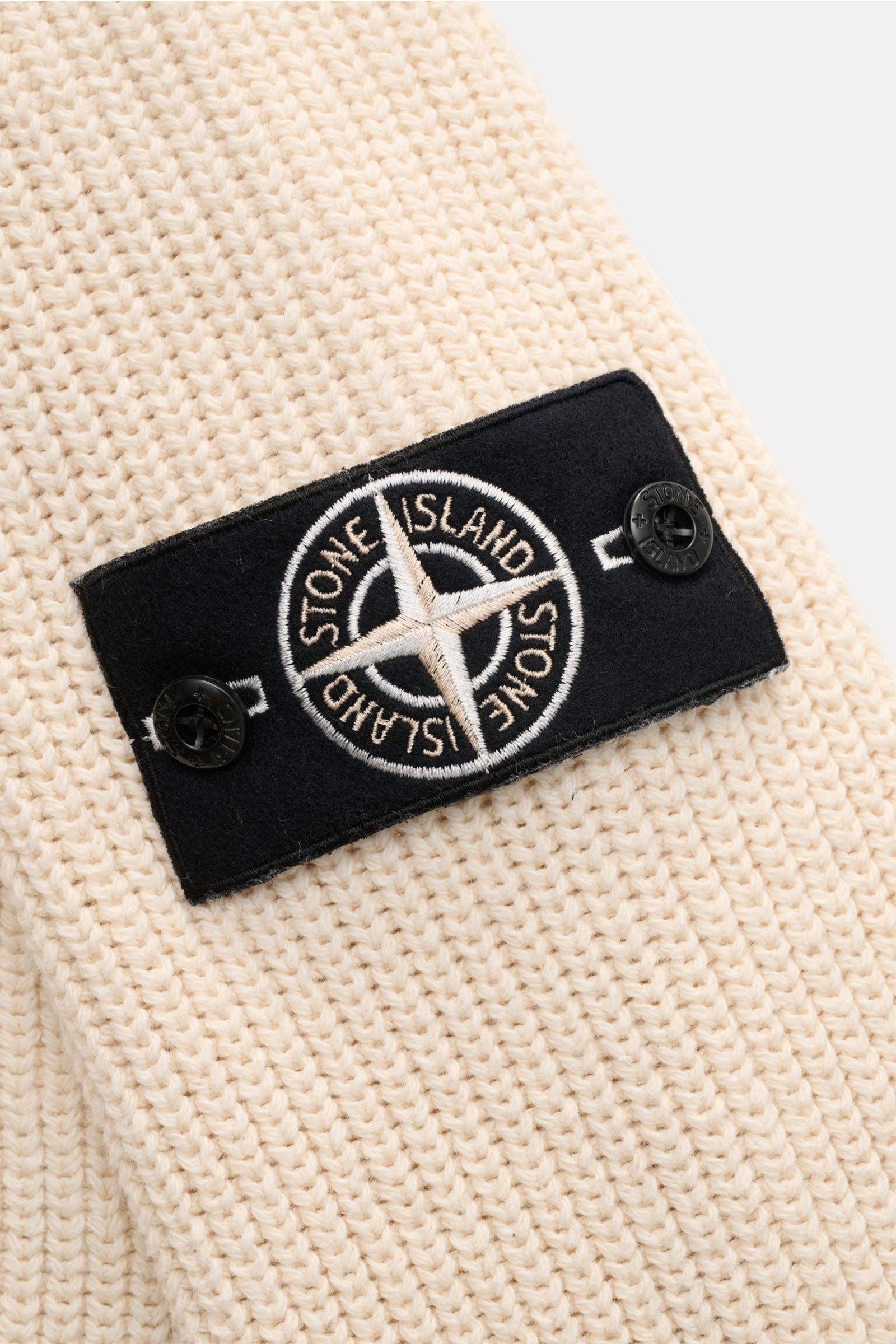 Close-up view of the Stone Island Strickjacke 'Raw Beauty' creme showing the black compass badge on cream patent cotton knit. 

Ein Essential für moderne Casual-Looks: Diese Strickjacke von STONE ISLAND überzeugt mit markantem Patentstrick aus reiner B