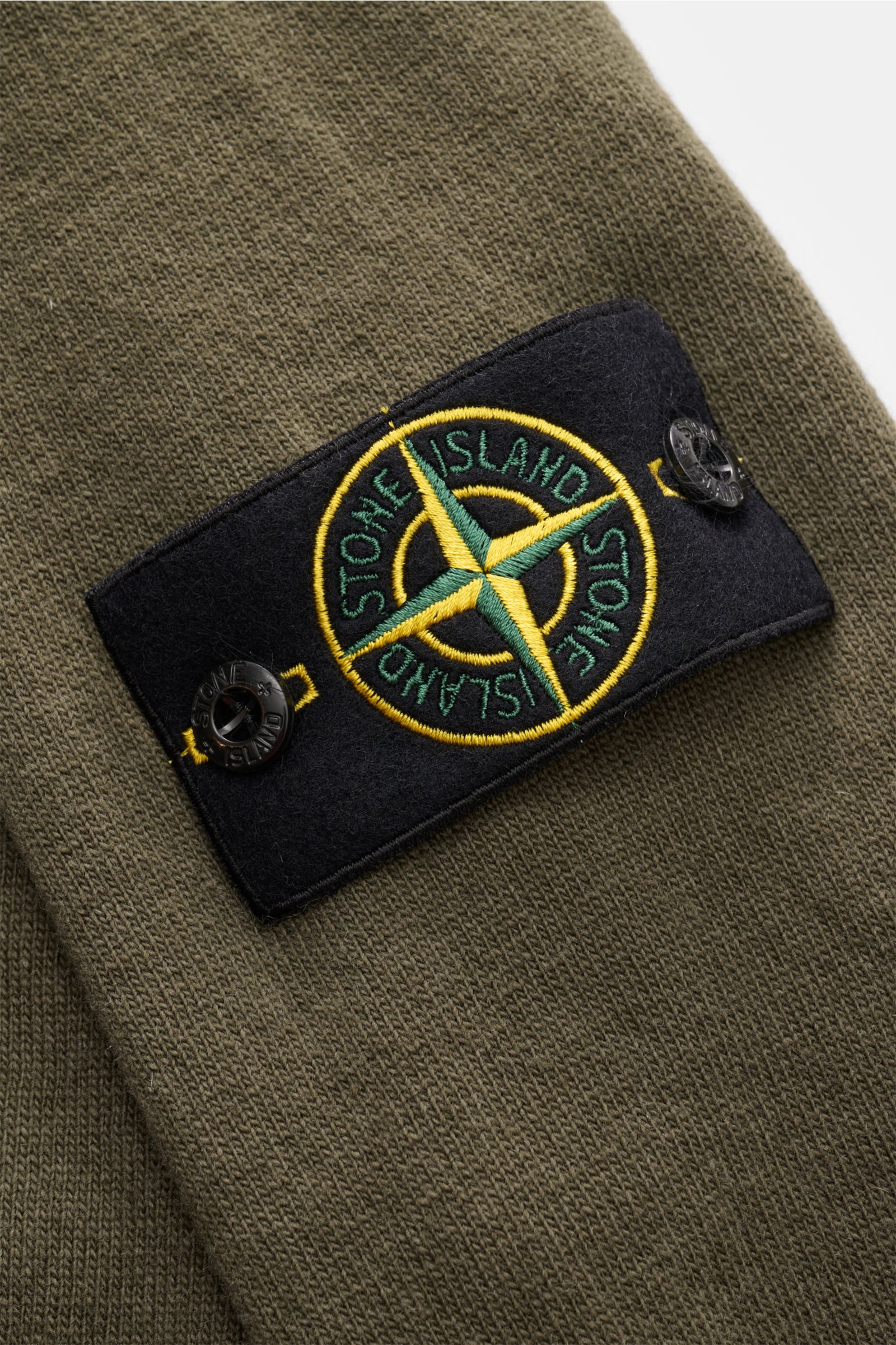 Stone Island Strickjacke oliv, Detailaufnahme des Kompass-Badges auf Raglanärmel, feinste Geelong-Schurwolle, RWS-zertifiziert, Slim Fit, Zwei-Wege-Reißverschluss, Stehkragen, Rippbündchen.