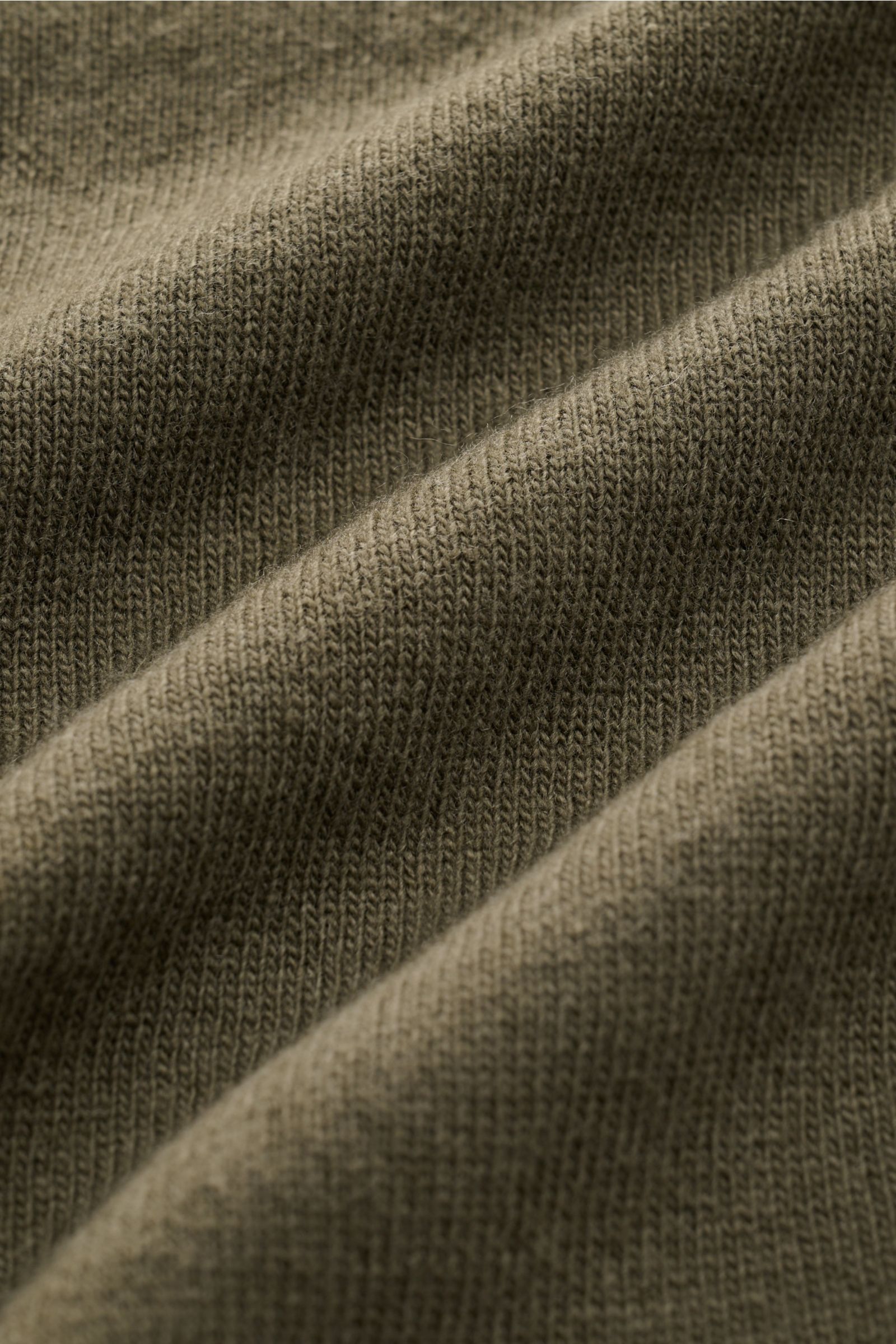 Nahaufnahme der olivfarbenen Stone Island Strickjacke, Detail des feinen Geelong-Schurwoll-Stoffs mit weichem Griff und Jersey-Qualität.