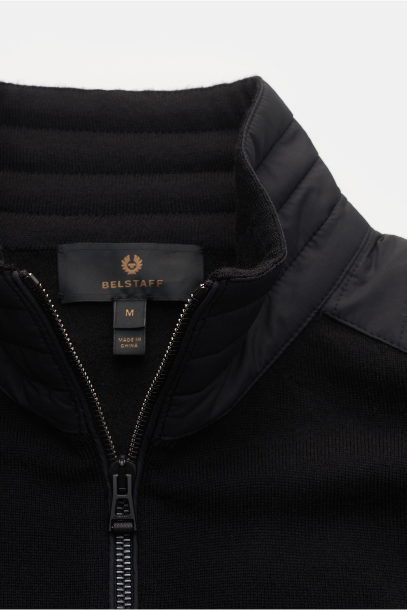 Close-up front view of Belstaff Strickjacke 'Kelby' schwarz showing quilted shoulder and collar details, two-way zipper, and knit texture.

Description: Bei BELSTAFF erinnert auch die Strickjacke 'Kelby' an die Wurzeln des Labels: Steppdetails an Schul