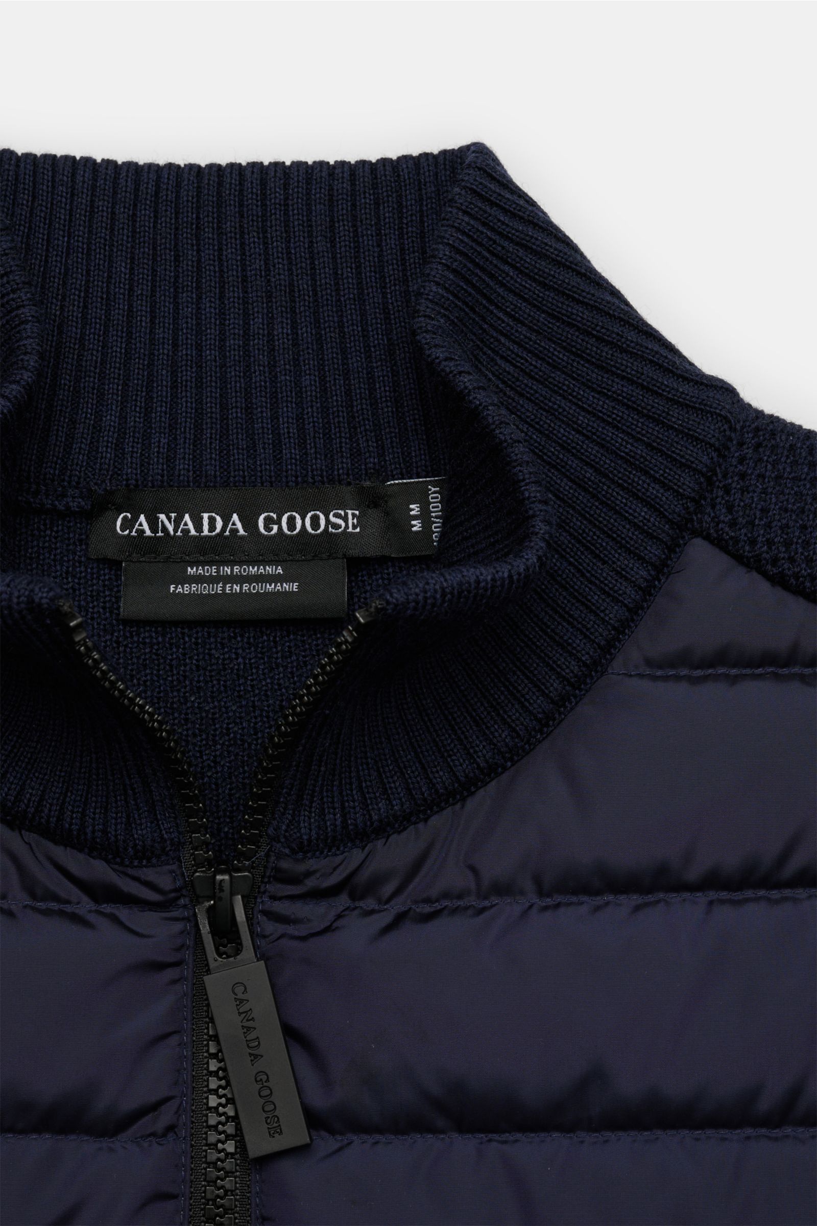 Nahaufnahme der Canada Goose Strickjacke 'Hybridge Knit' navy mit Daunen-Front, hochschließendem Stehkragen und robustem Reißverschluss, von oben fotografiert.