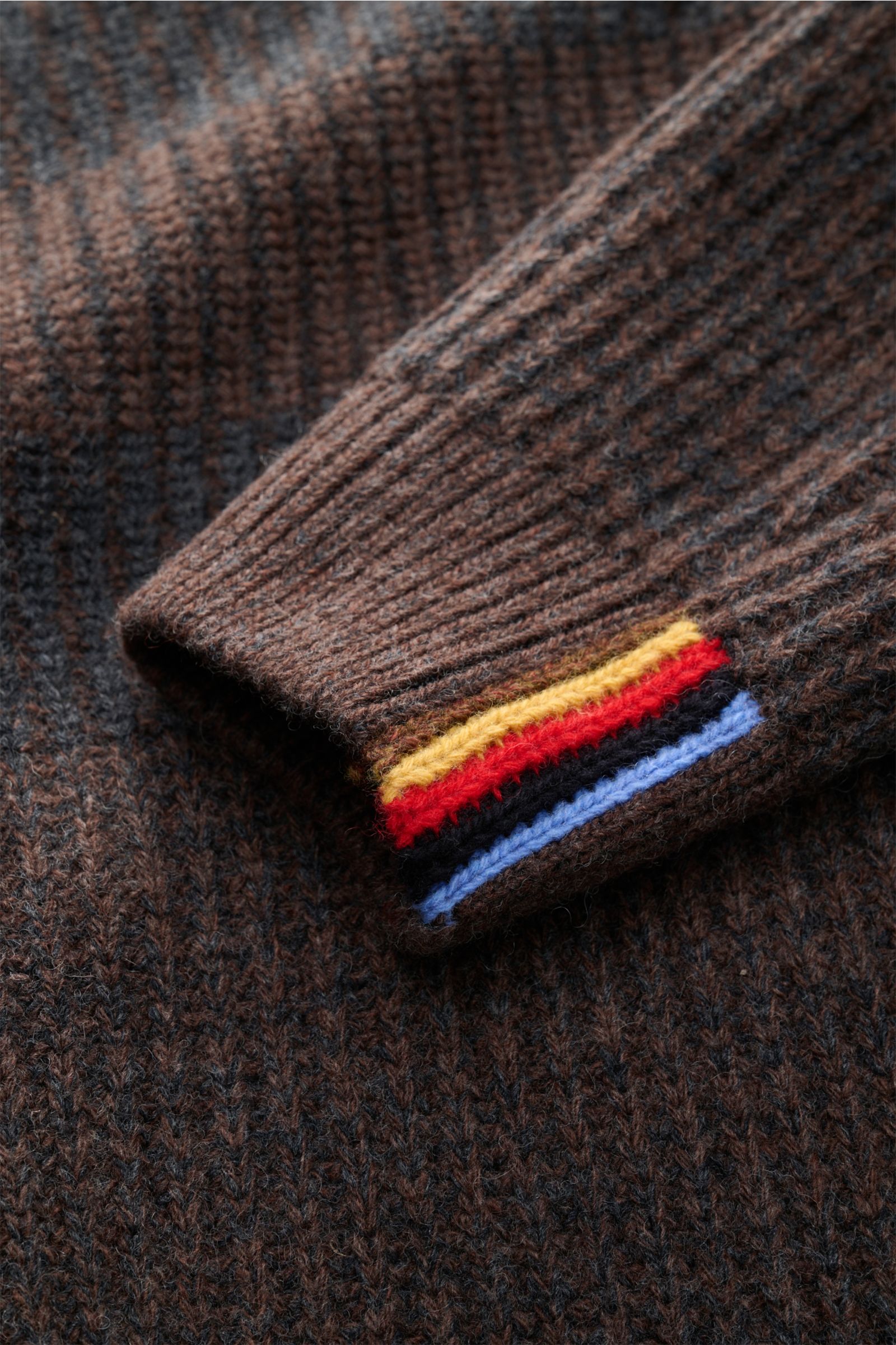 Nahaufnahme der Barbour Strickjacke 'Knit Bomber' dunkelbraun/dunkelgrau gestreift, Detail des Ärmelbündchens mit bunten Streifen, voluminöses Patent-Strickmuster, reine Wolle, weicher Griff.