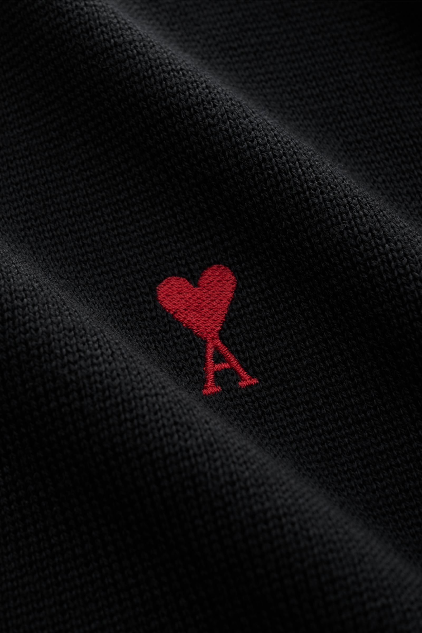 Nahaufnahme des schwarzen Ami Paris Merino Cardigan mit rotem 'Ami de Cœur' Monogramm auf der Brust, feines Merinowollstrickbild.