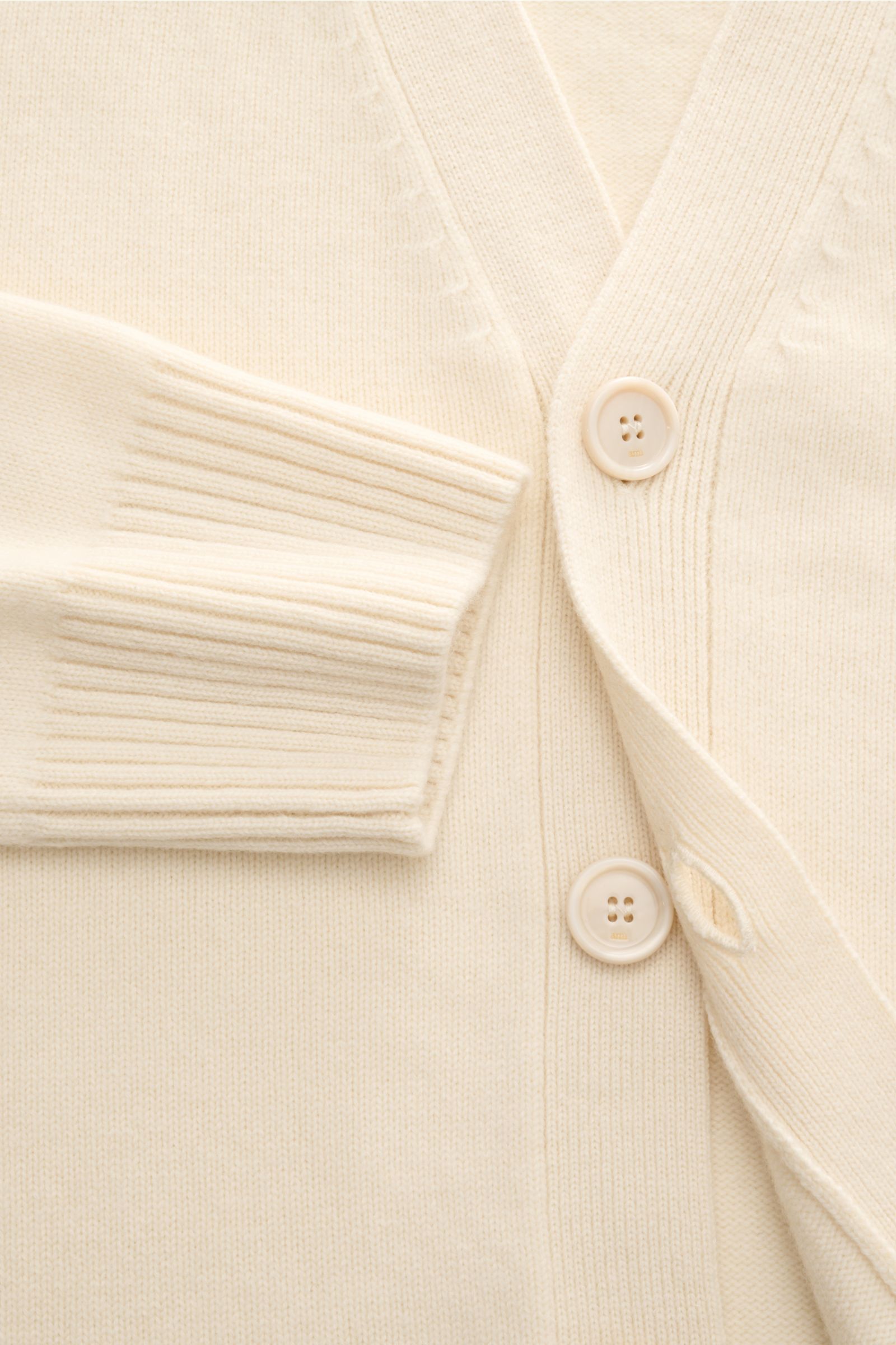 Close-up front view of Ami Paris Cardigan cream showcasing wool and cashmere knit, soft feel, medium-fine knit, oversized fit, four-button placket, V-neck, wide elasticated ribbed bands, and quilted 'Ami' logo.